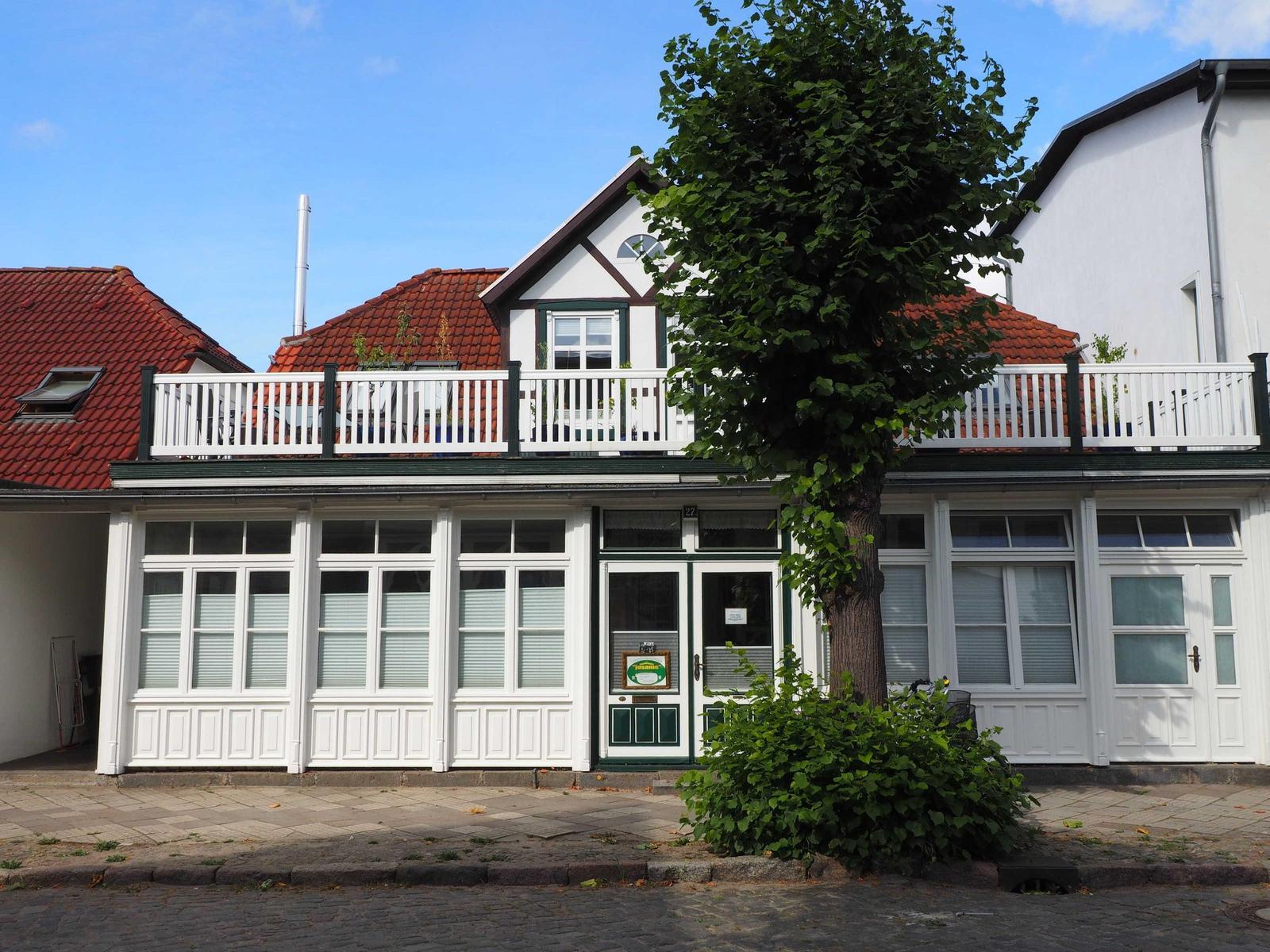 Haus mit weißem Balkon, rotem Dach und großen Fenstern an der Straße