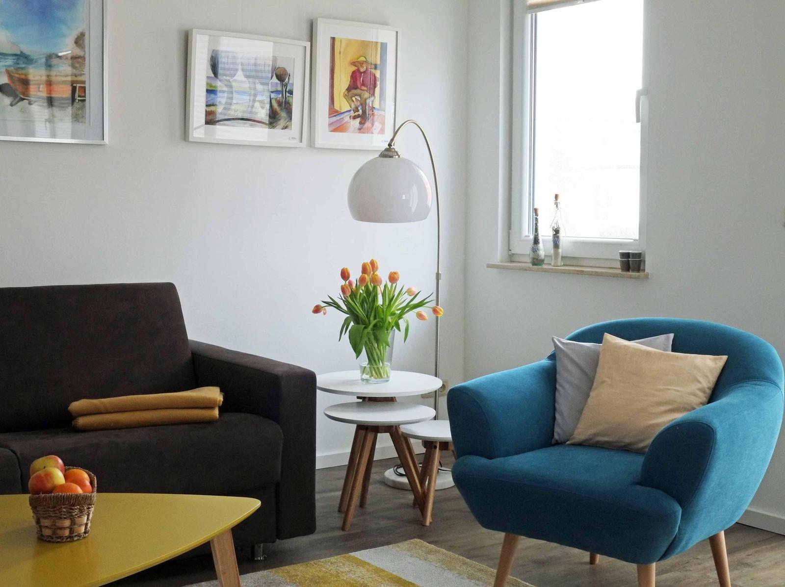 Ein Wohnzimmer mit Sofa, blauem Sessel, Tisch und Blumen.