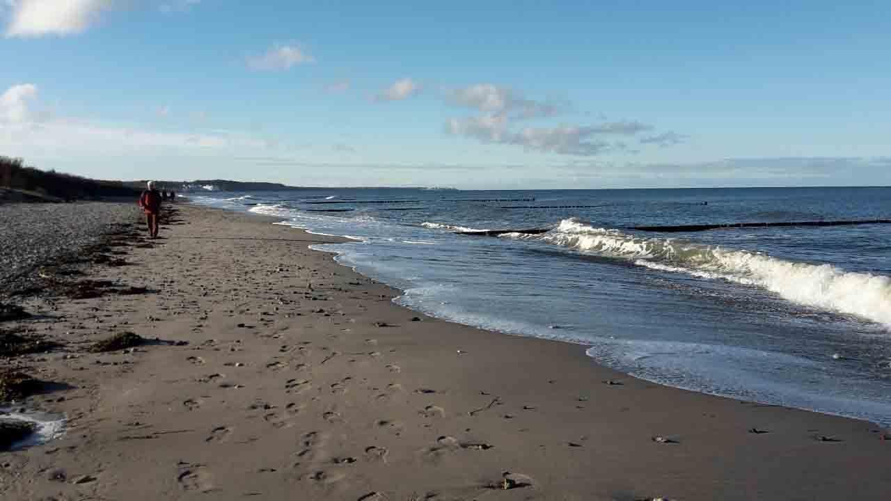 Strand mit Wellen und Spuren, ein Wanderer geht entlang des Wassers.