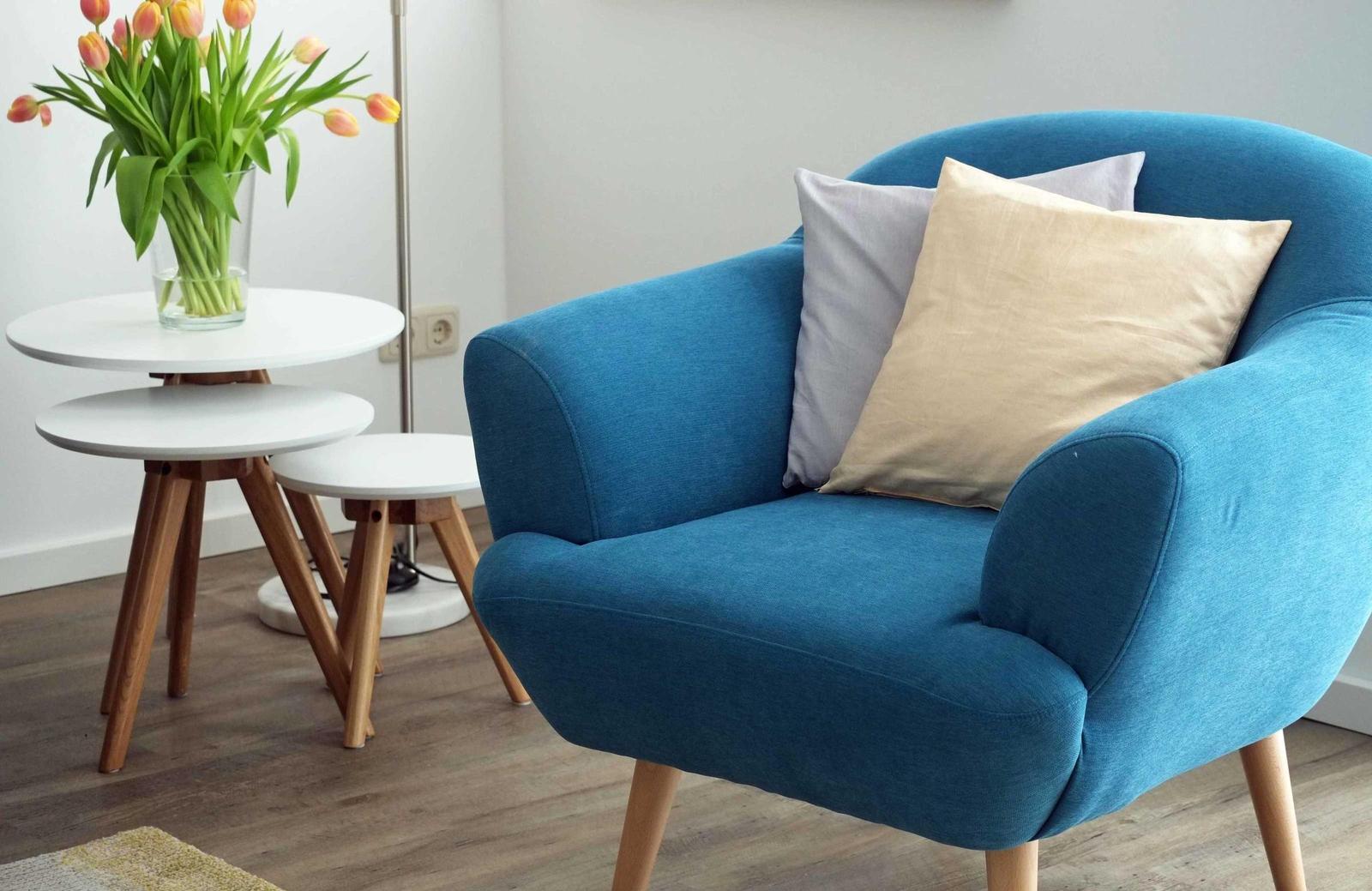 Ein blauer Sessel mit Kissen steht neben einem weißen Tisch mit Tulpen.