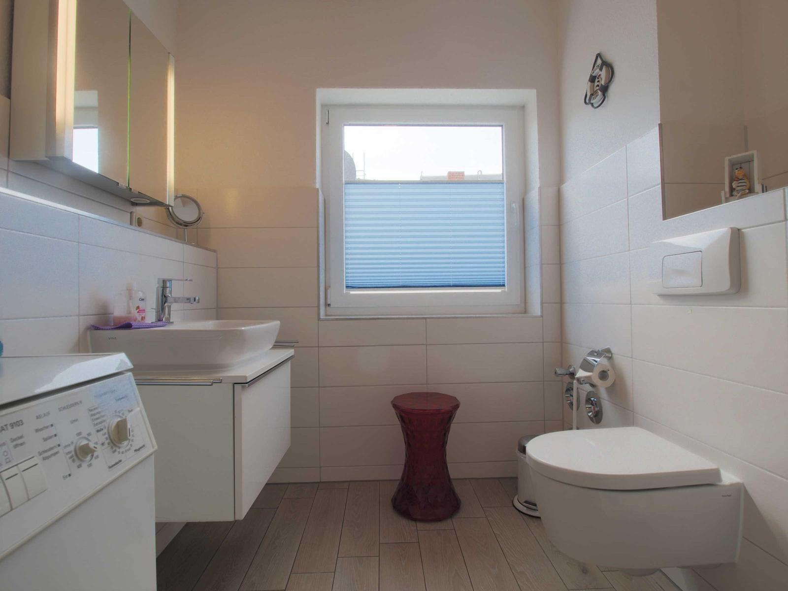 Badezimmer mit Waschbecken, Toilette und Fenster mit Jalousie.