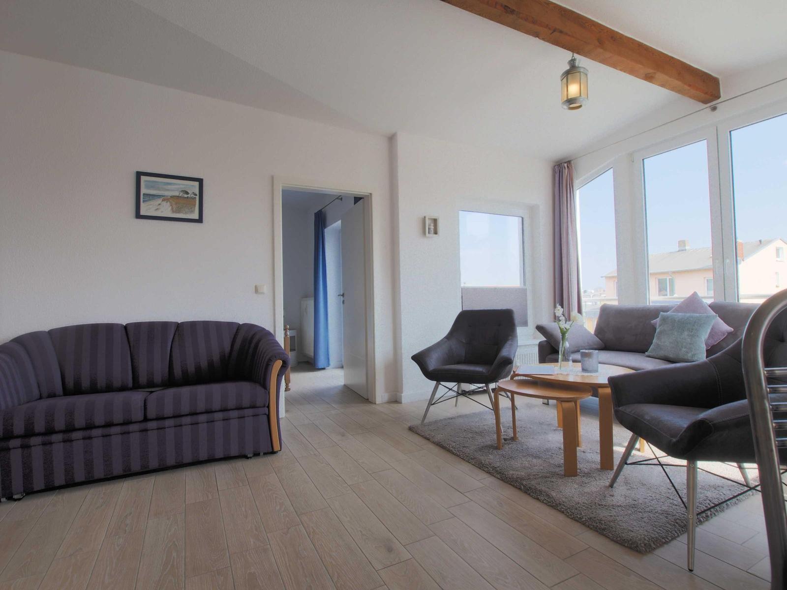 Wohnzimmer mit Sofa, Sessel und Tisch. Holzboden und große Fenster.