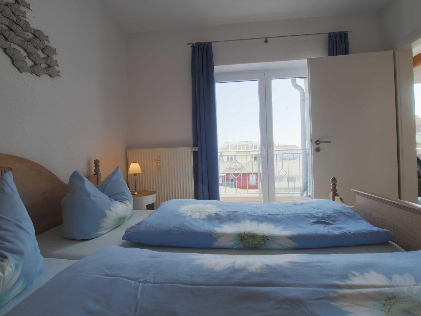 Schlafzimmer mit Bett, Vorhang und Balkontür. Wanddekoration mit Fischmotiv.