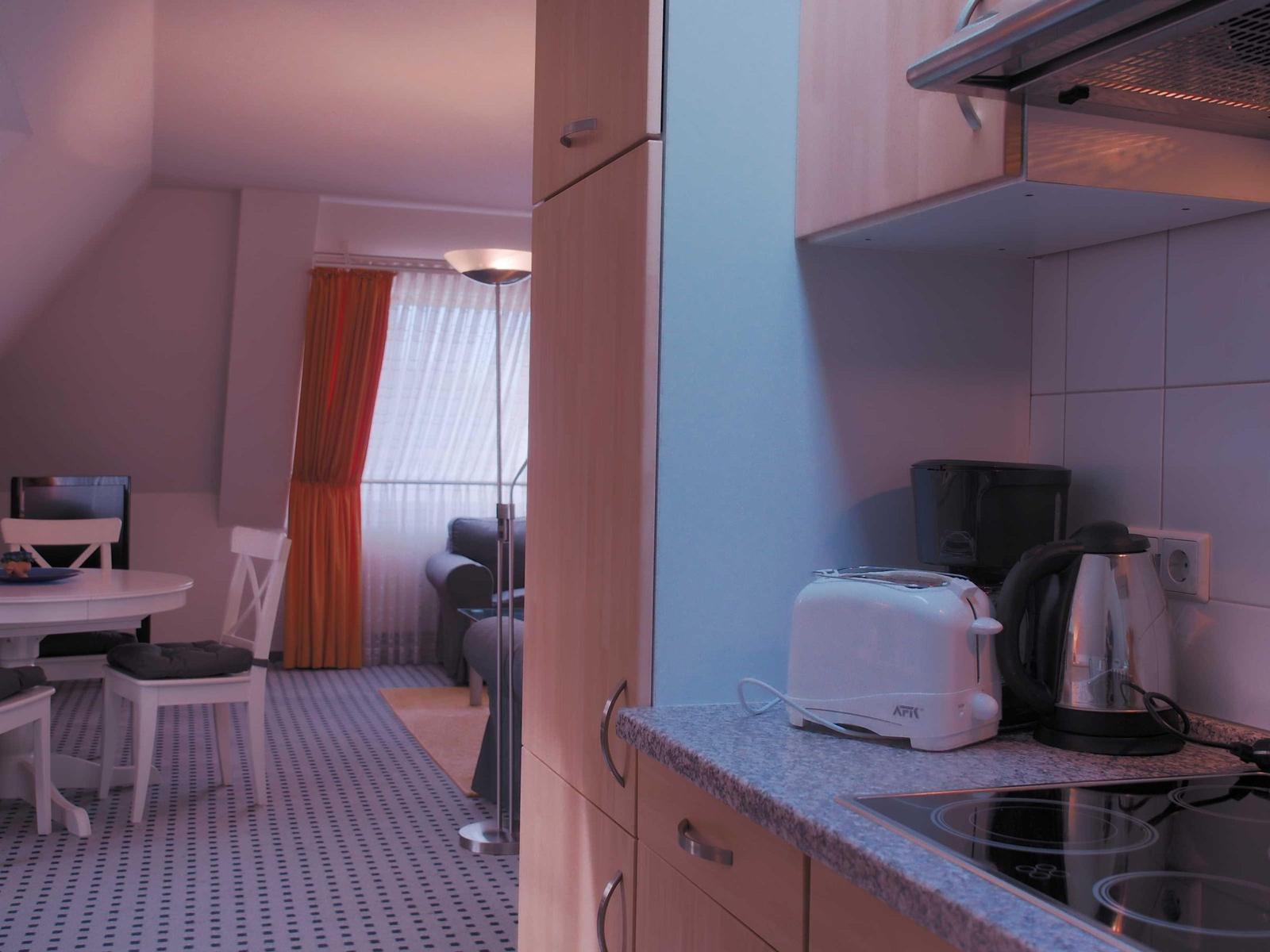 Küche mit Toaster und Kaffeemaschine. Blick in Wohnbereich mit Tisch, Stühlen und Sofa.
