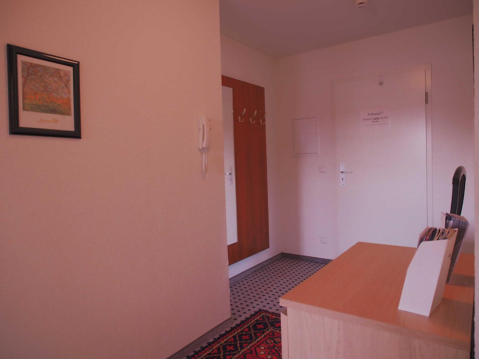 Eingangsbereich mit Wandbild, Telefon, Garderobe und Tür mit Achtungsaufkleber.
