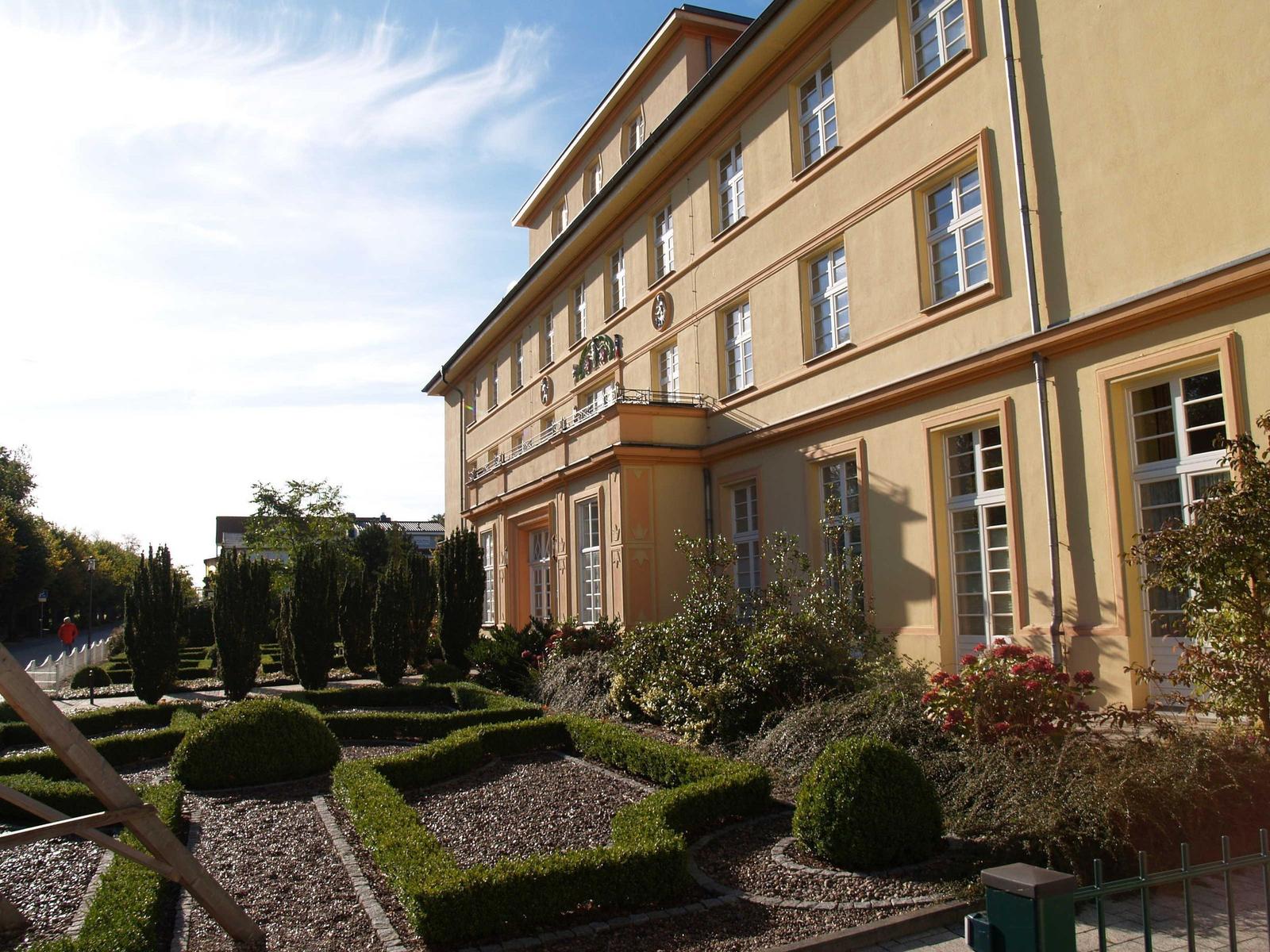Ein gelbes Gebäude mit Fenstern und einem gepflegten Garten mit Hecken und Blumen.