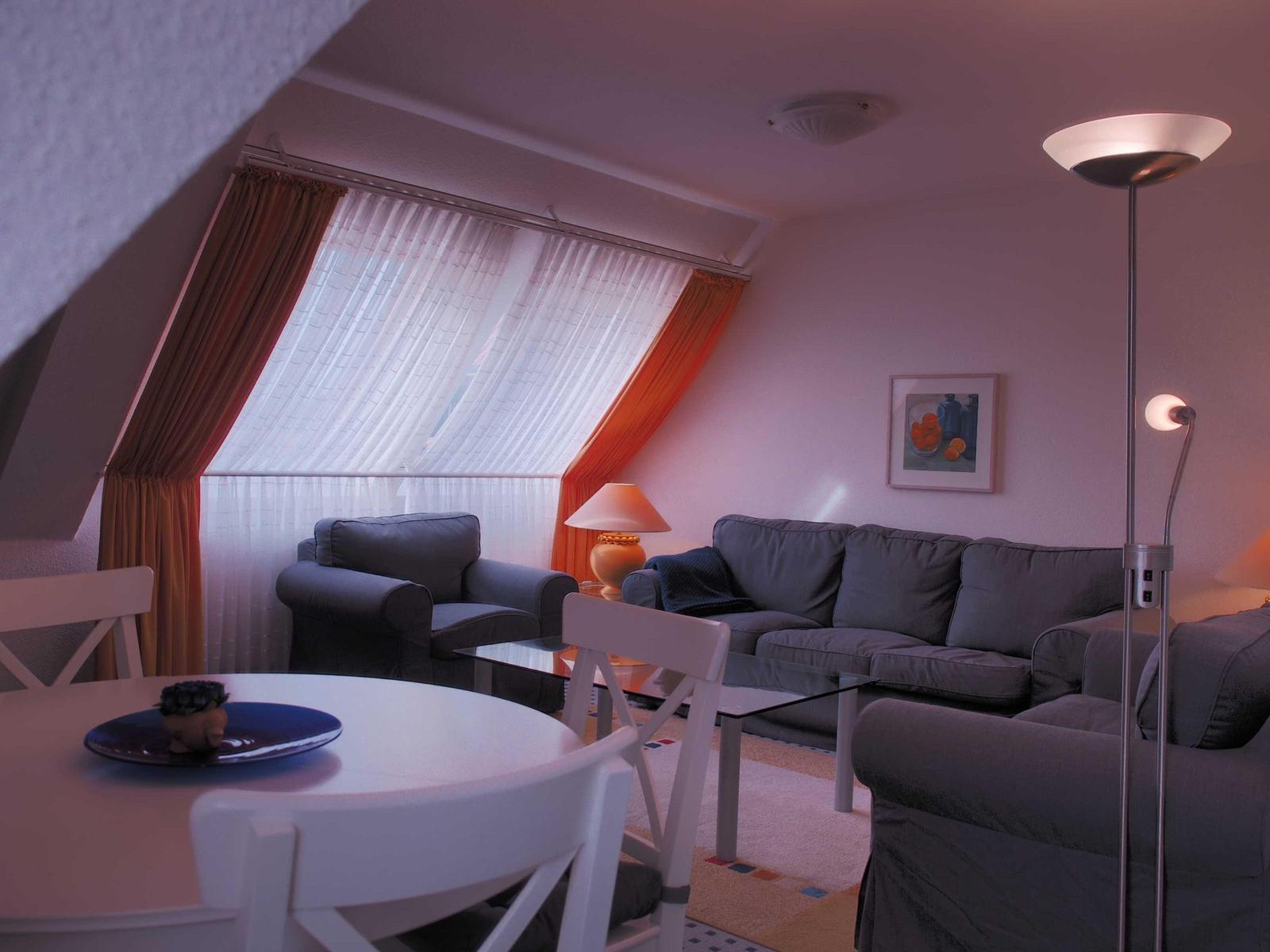 Wohnzimmer mit Sofa, Sessel, Esstisch und Fenster mit Vorhängen.