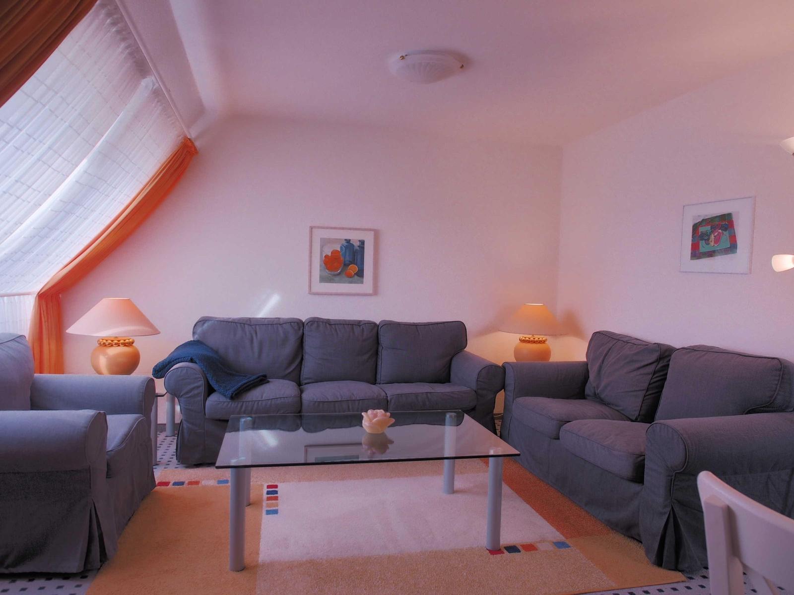 Wohnzimmer mit grauen Sofas, Glas-Tisch und Fenster mit Vorhängen.