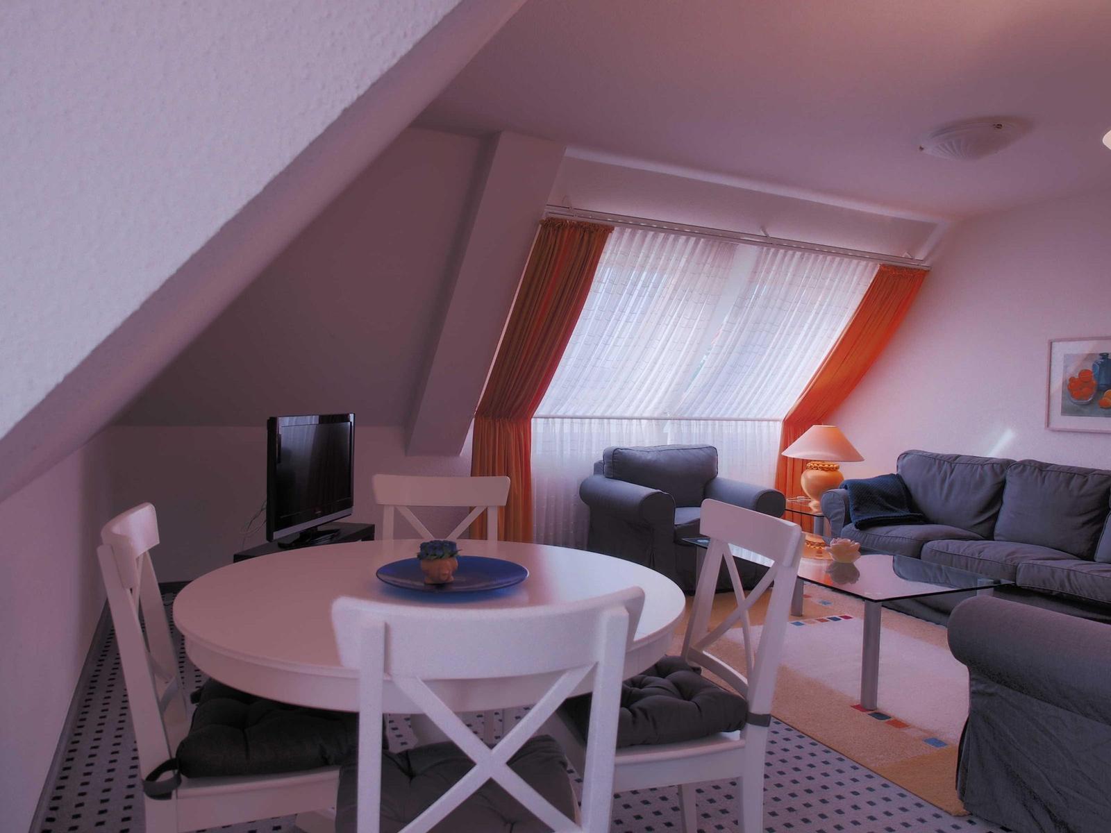 Wohn- und Essbereich mit Sofa, Esstisch und TV unter Dachschräge.