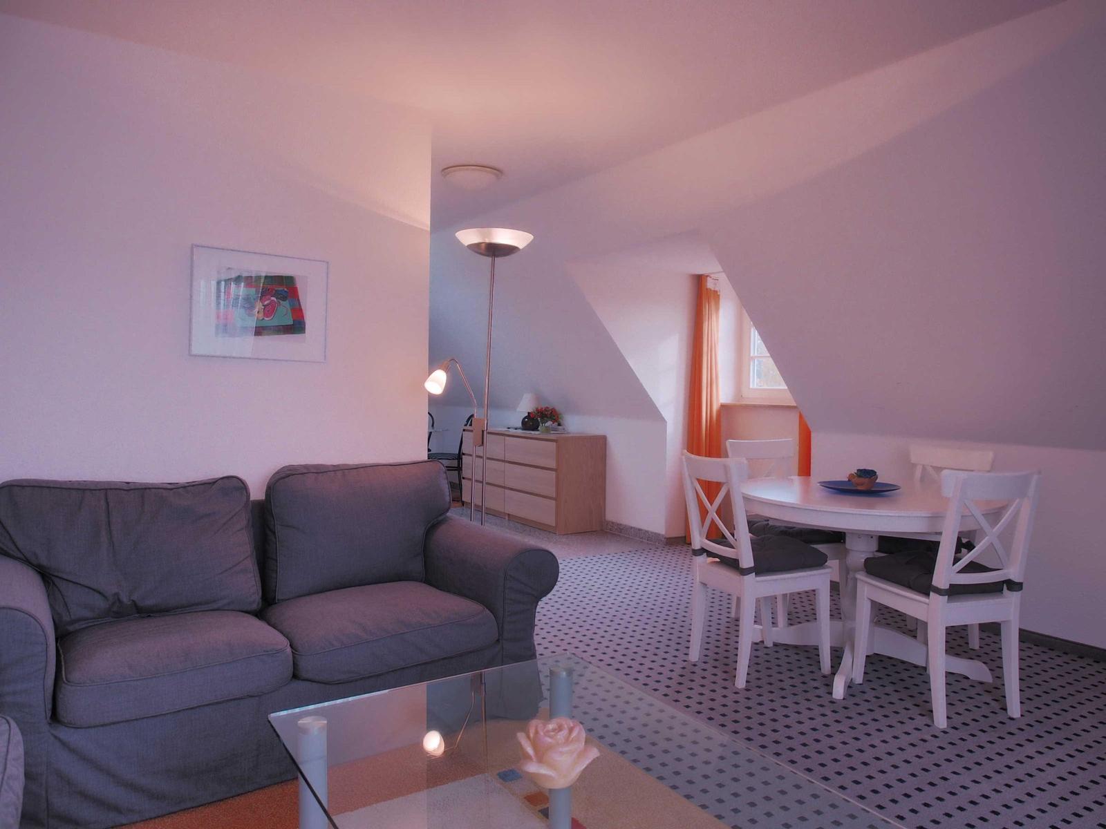 Wohn- und Essbereich mit Sofa, Tisch und Stühlen sowie schrägen Wänden.