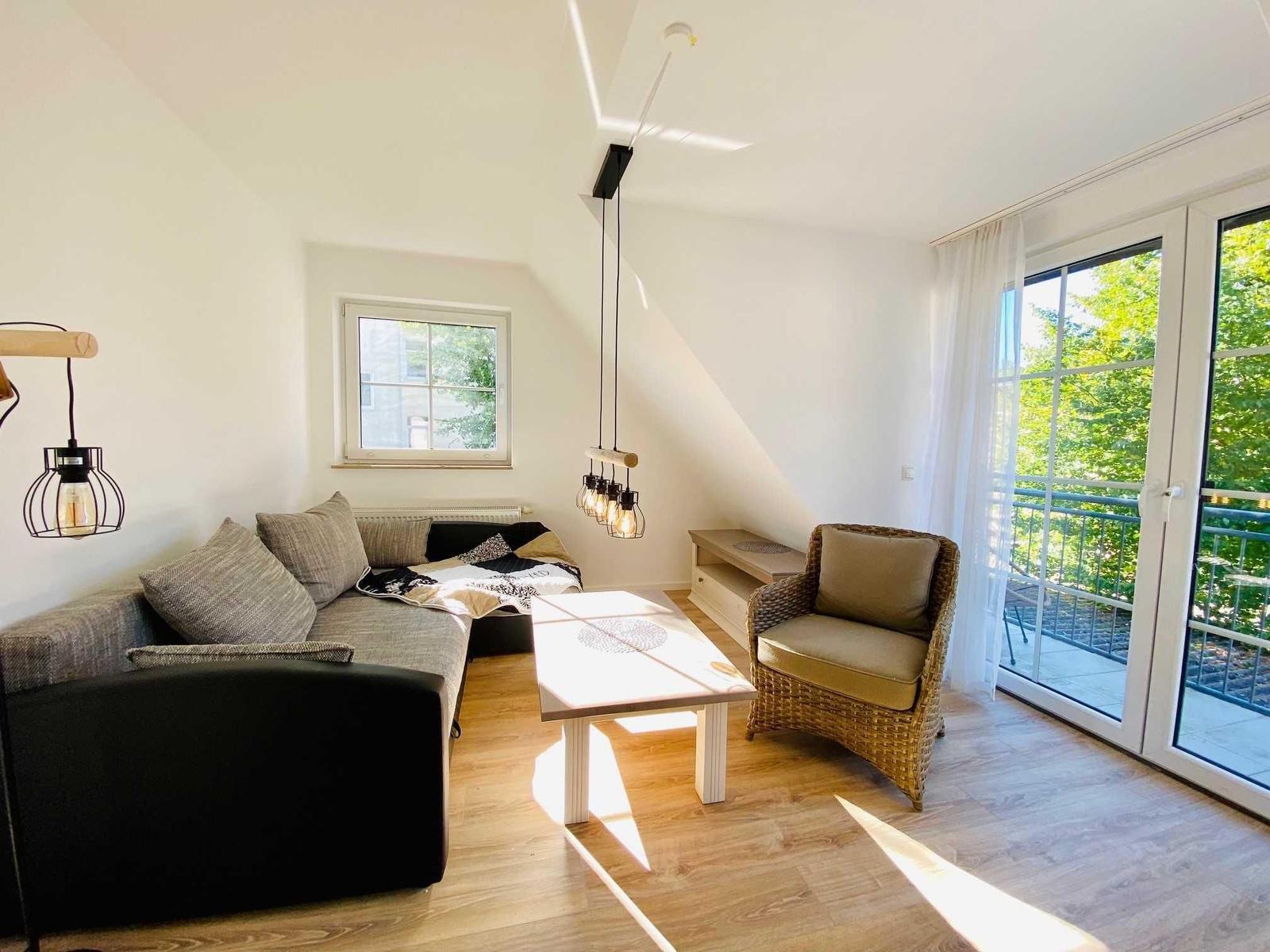 Wohnzimmer mit Sofa, Sessel und Balkon. Holzboden und Dachschrägen.
