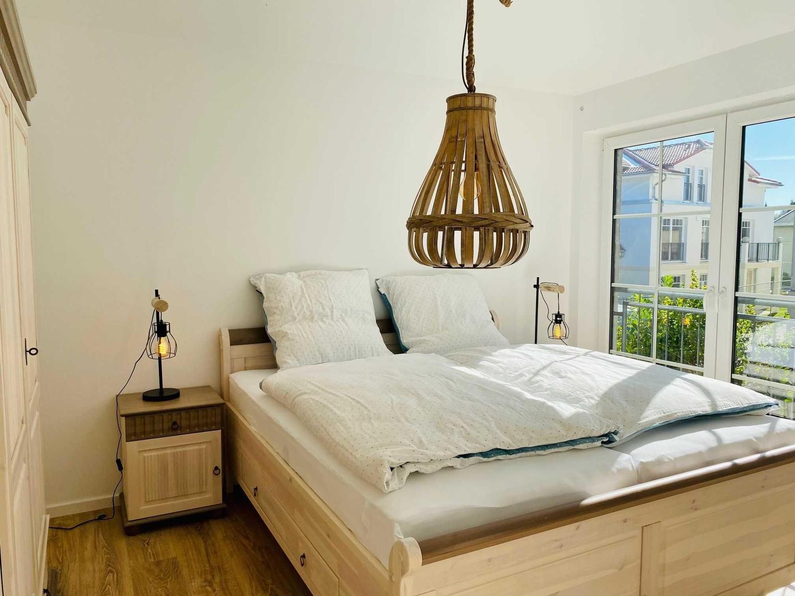 Schlafzimmer mit Doppelbett, Holzfußboden und Balkontür. Holzlampe hängt über dem Bett.