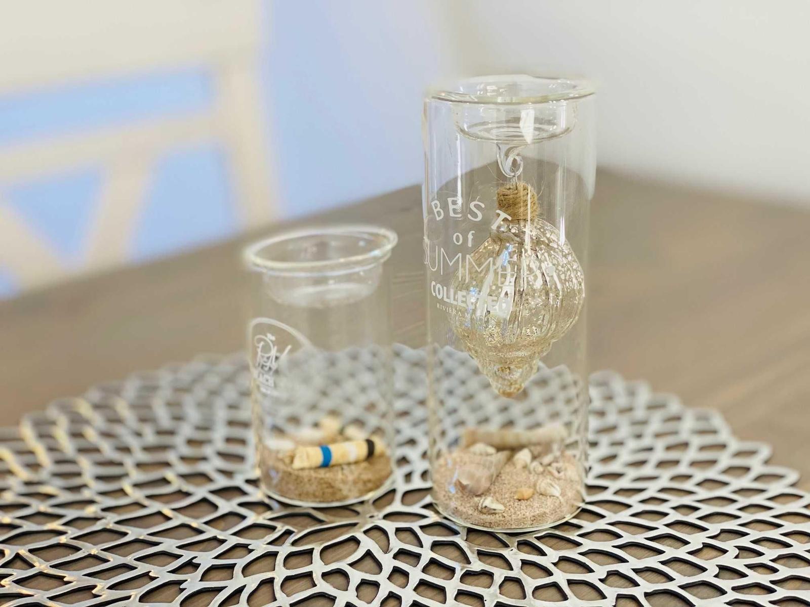 Zwei Glasbehälter mit Sand und Muscheln auf einem Metalltablett.