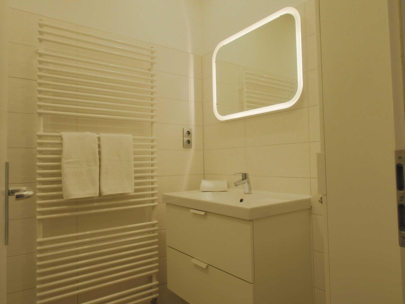 Badezimmer mit Waschtisch, Spiegel und Handtuchhalter.