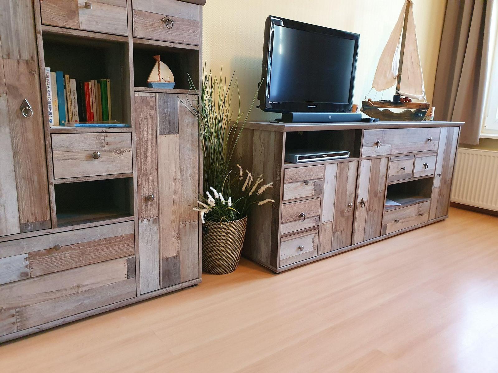 TV-Schrank mit Fernseher, Modellboot und Pflanze. Holzmöbel und hellbrauner Boden.