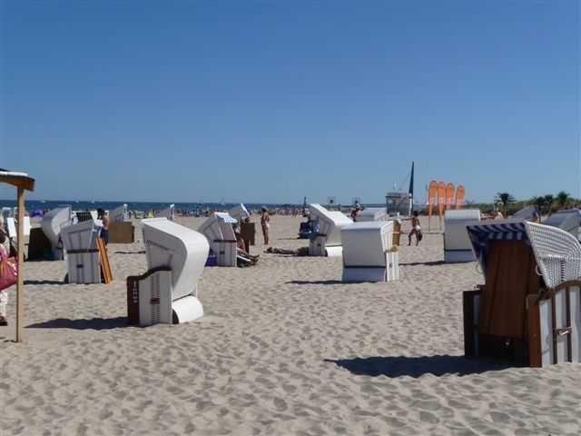 Strand mit weißen Strandkörben und Menschen unter blauem Himmel.