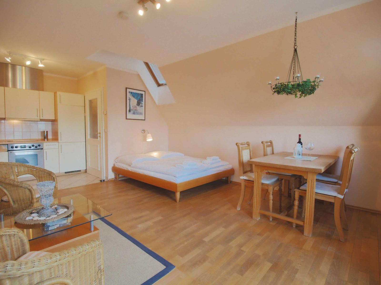 Ein Schlafzimmer mit Dachfenster, Esstisch, Küchenbereich und Wohnbereich mit Sitzgelegenheiten.
