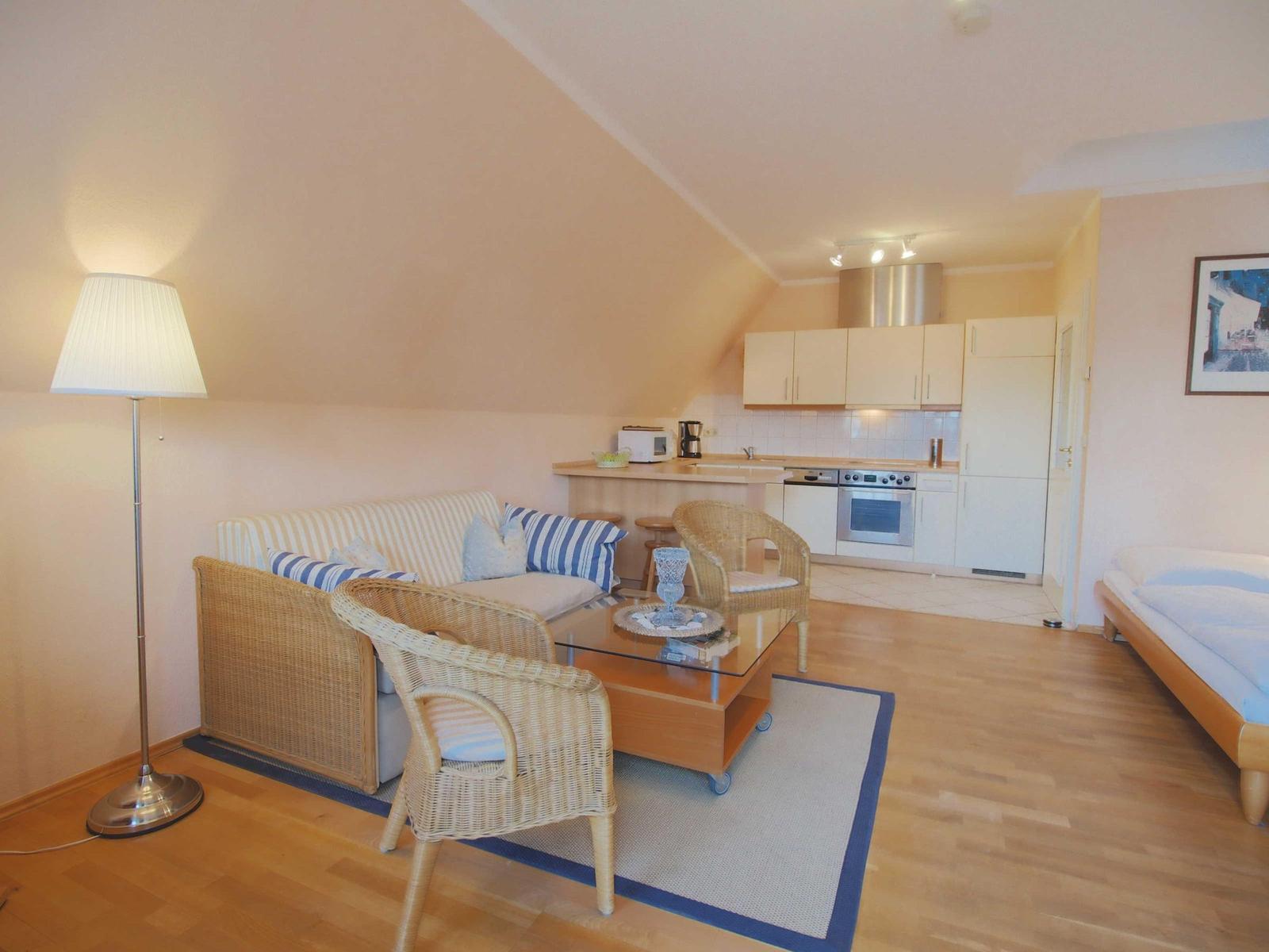 Wohnzimmer mit Sofa, Stühlen und Küchenbereich. Holzboden und Dachschräge.