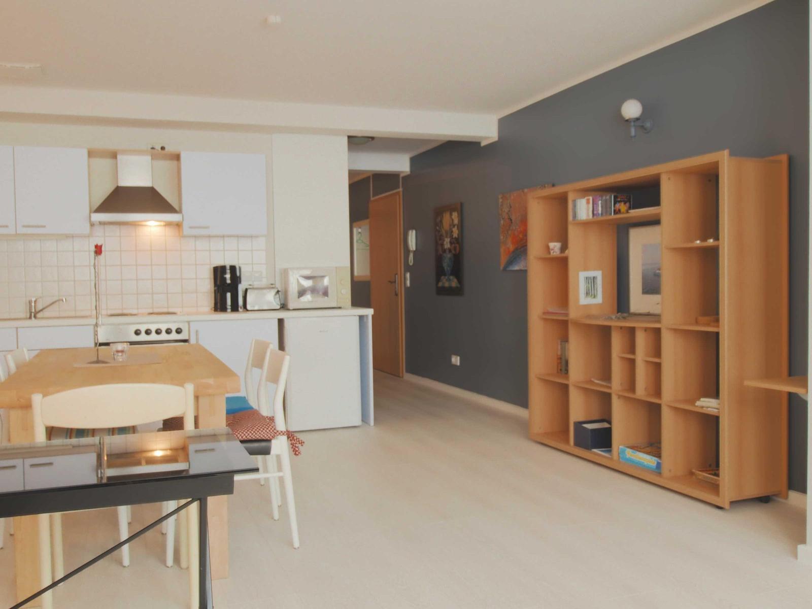 Küche mit Esstisch, Wohnbereich mit Bücherregal und grauer Wand.