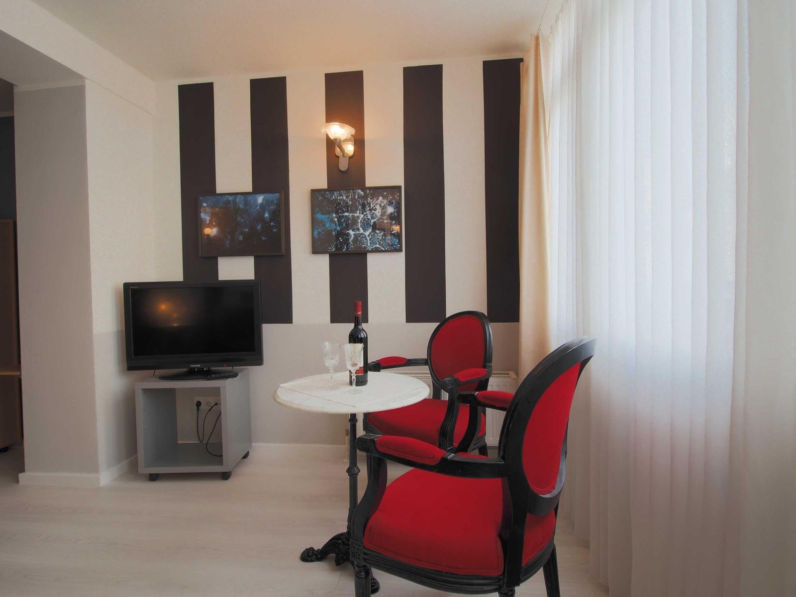 Zimmer mit zwei roten Stühlen, Tisch, Fernseher und Wandbildern.