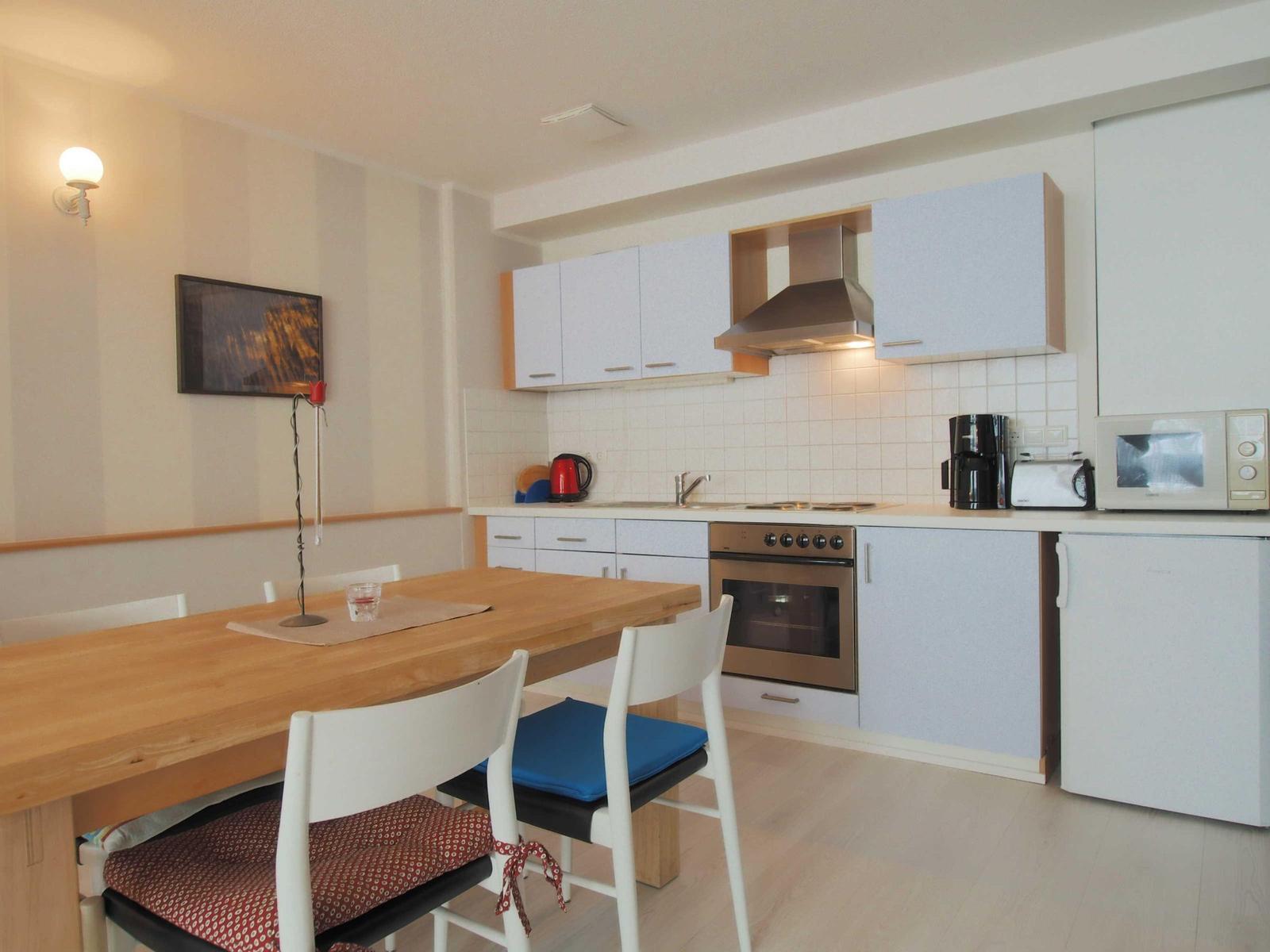 Küche mit Esstisch, Kühlschrank, Herd und Mikrowelle.
