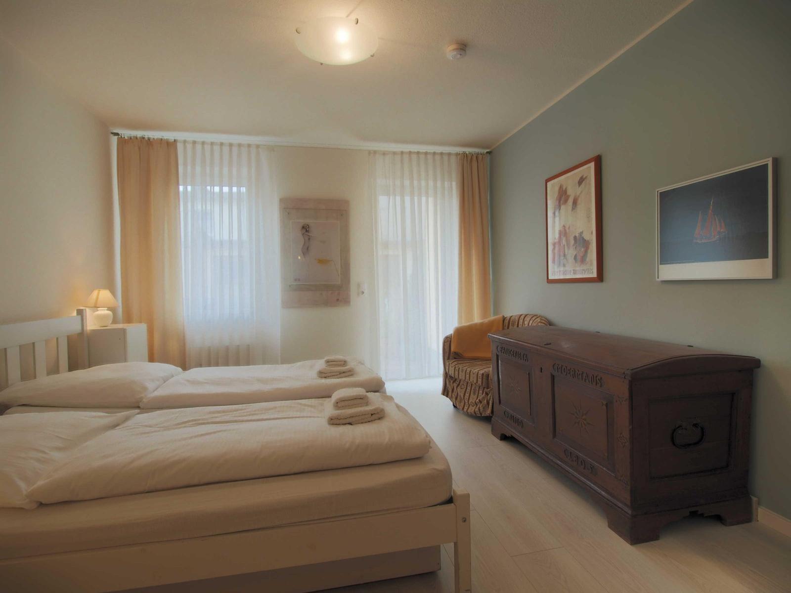 Zimmer mit Doppelbett, Holzschrank und Fenster mit Vorhängen.
