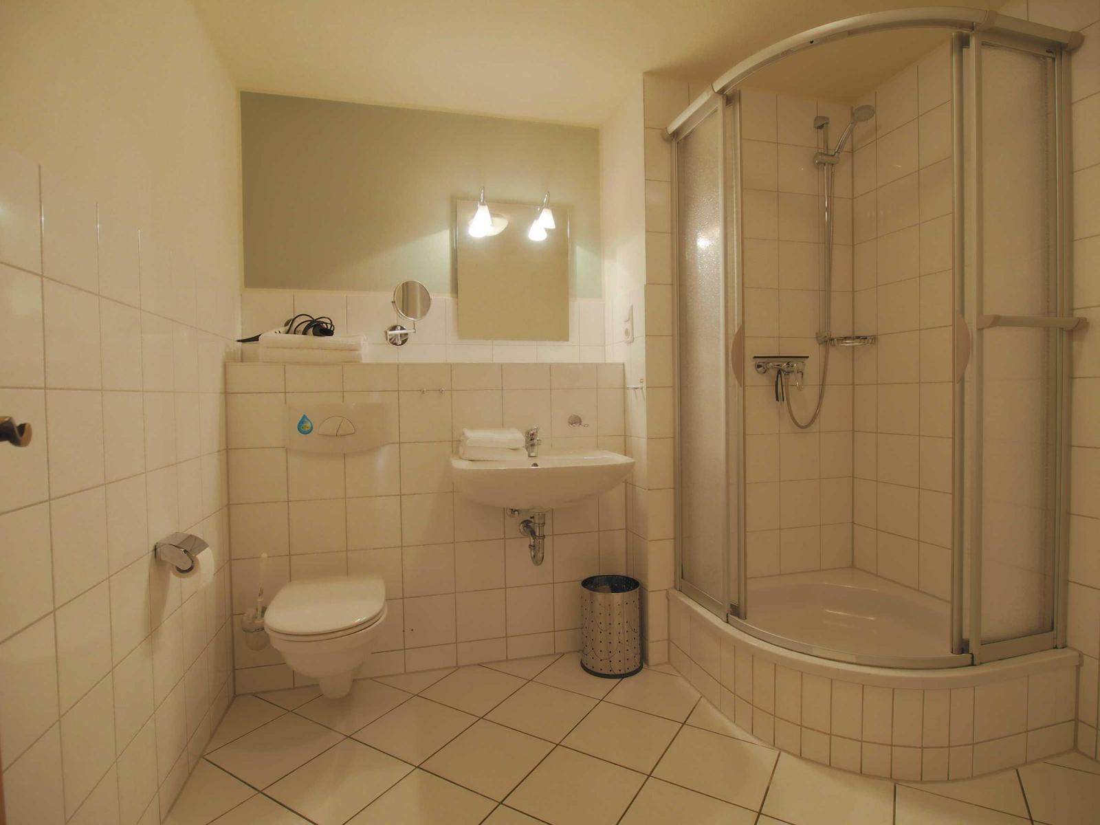 Badezimmer mit Dusche, Waschbecken und Toilette. Fliesenwand und Boden.