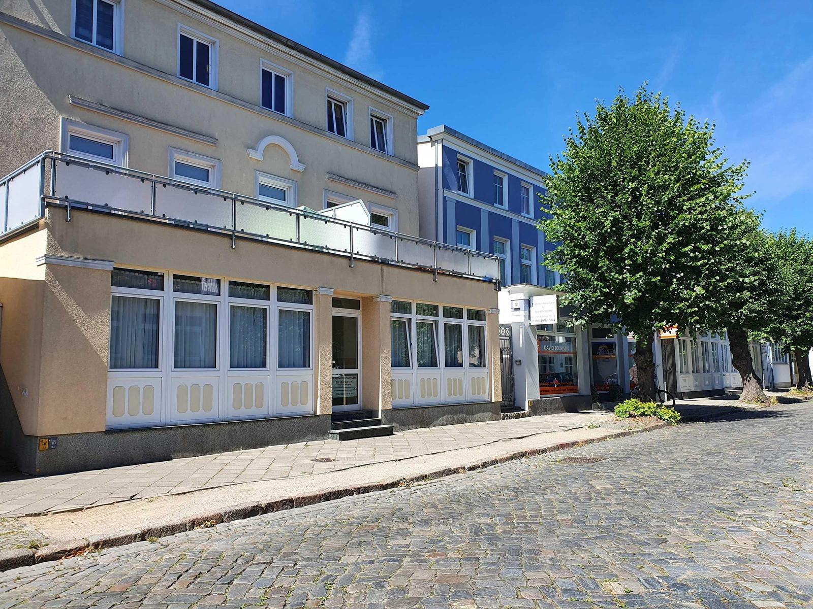 Fassade eines Ferienhauses mit Balkon und Fenstern an einer Straße mit Kopfsteinpflaster.