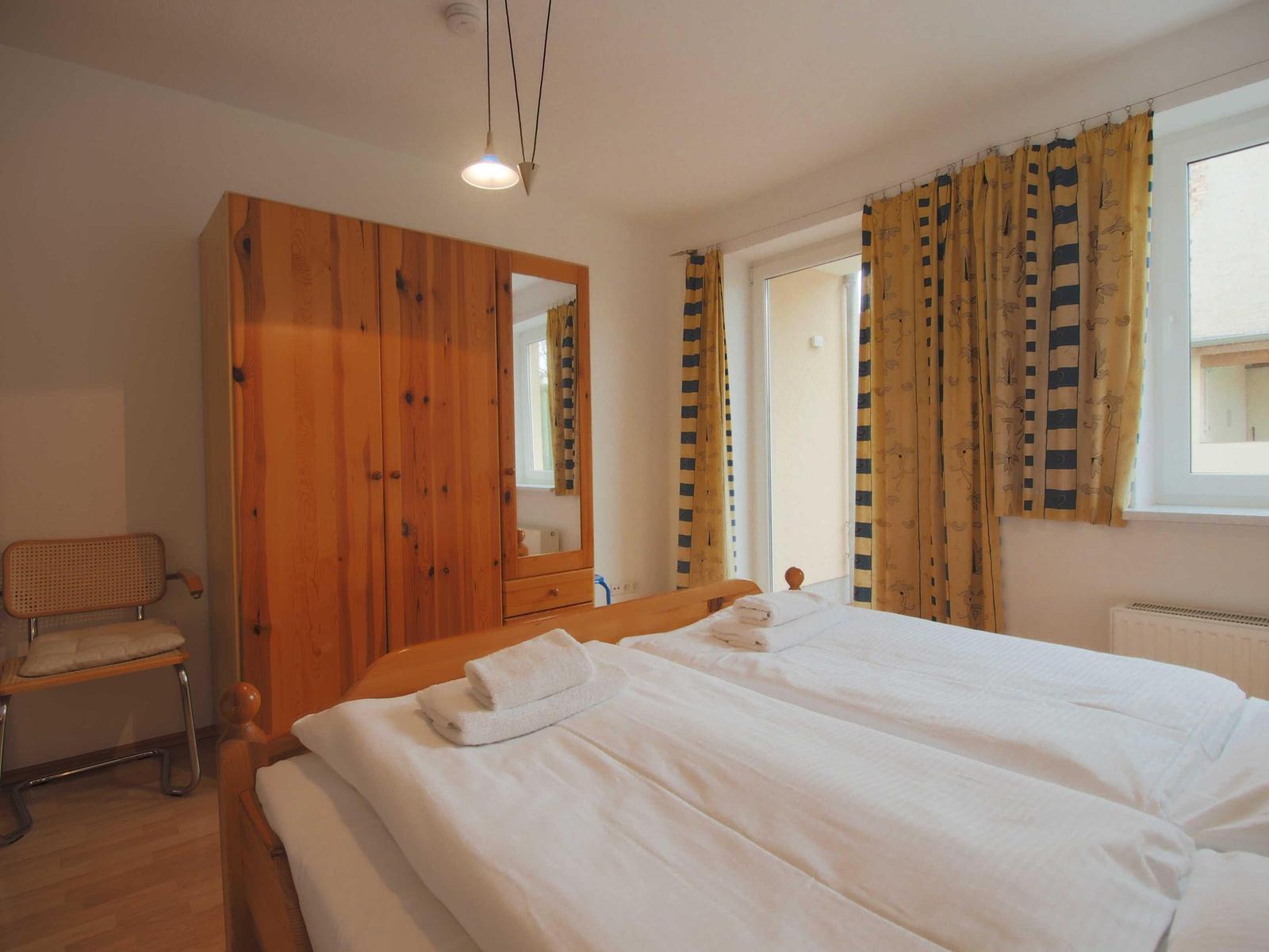 Schlafzimmer mit Doppelbett, Holzschrank und gelben Vorhängen.