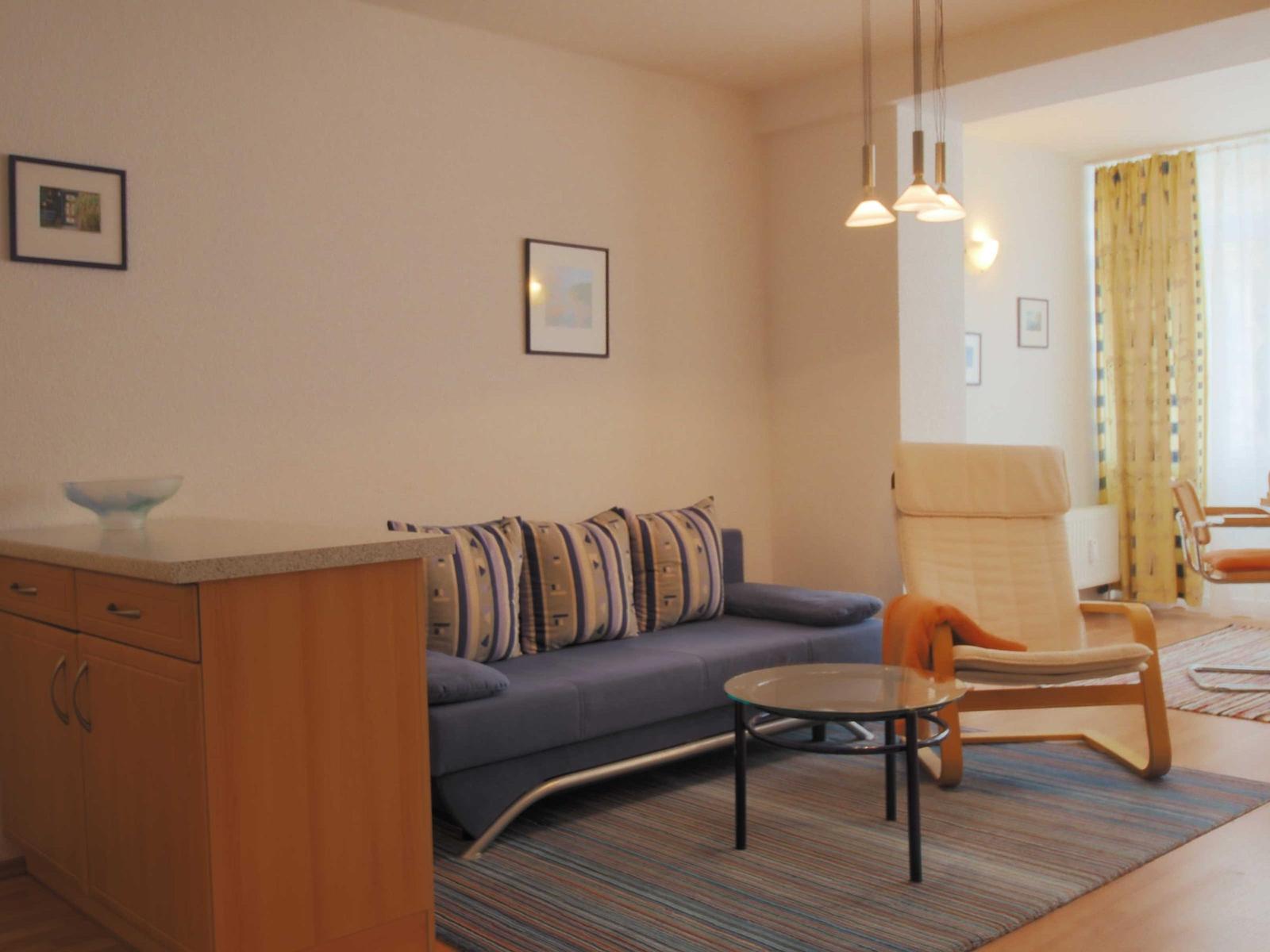 Wohnzimmer mit Sofa, Sessel und Couchtisch. Helle Wände und Holzmöbel.