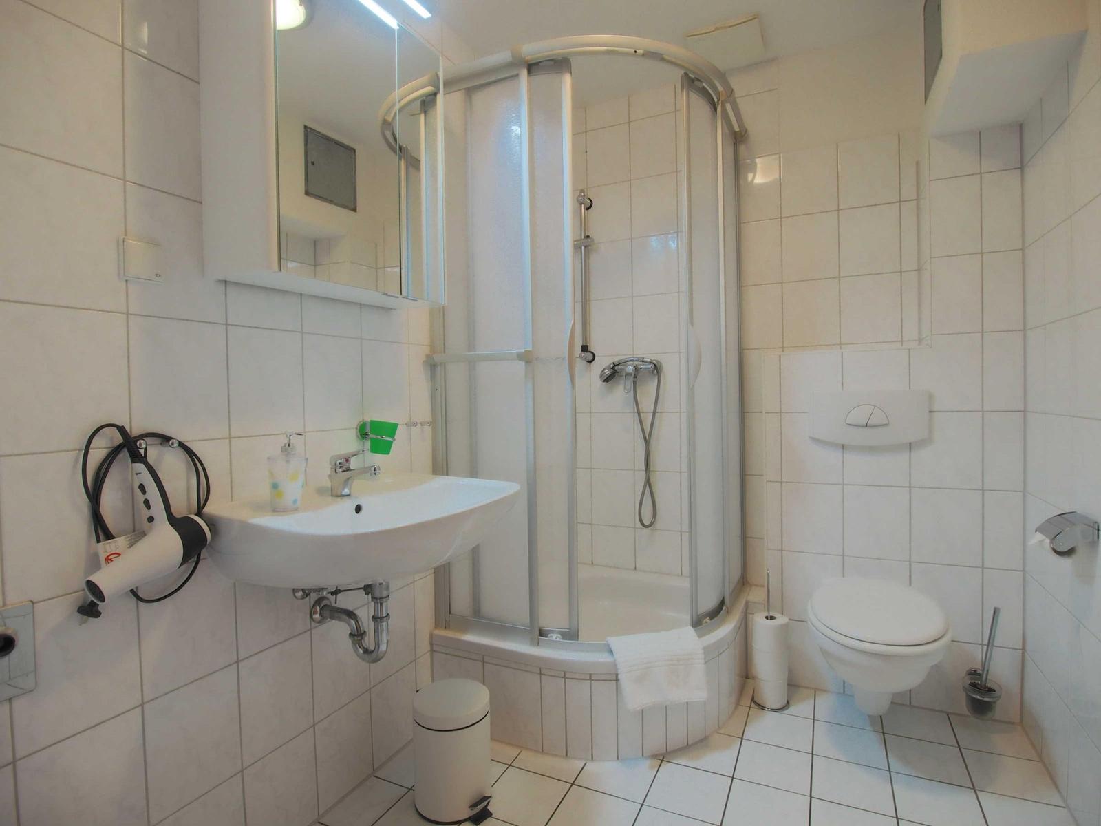 Badezimmer mit Dusche, Waschbecken und Toilette. Trockner an der Wand.