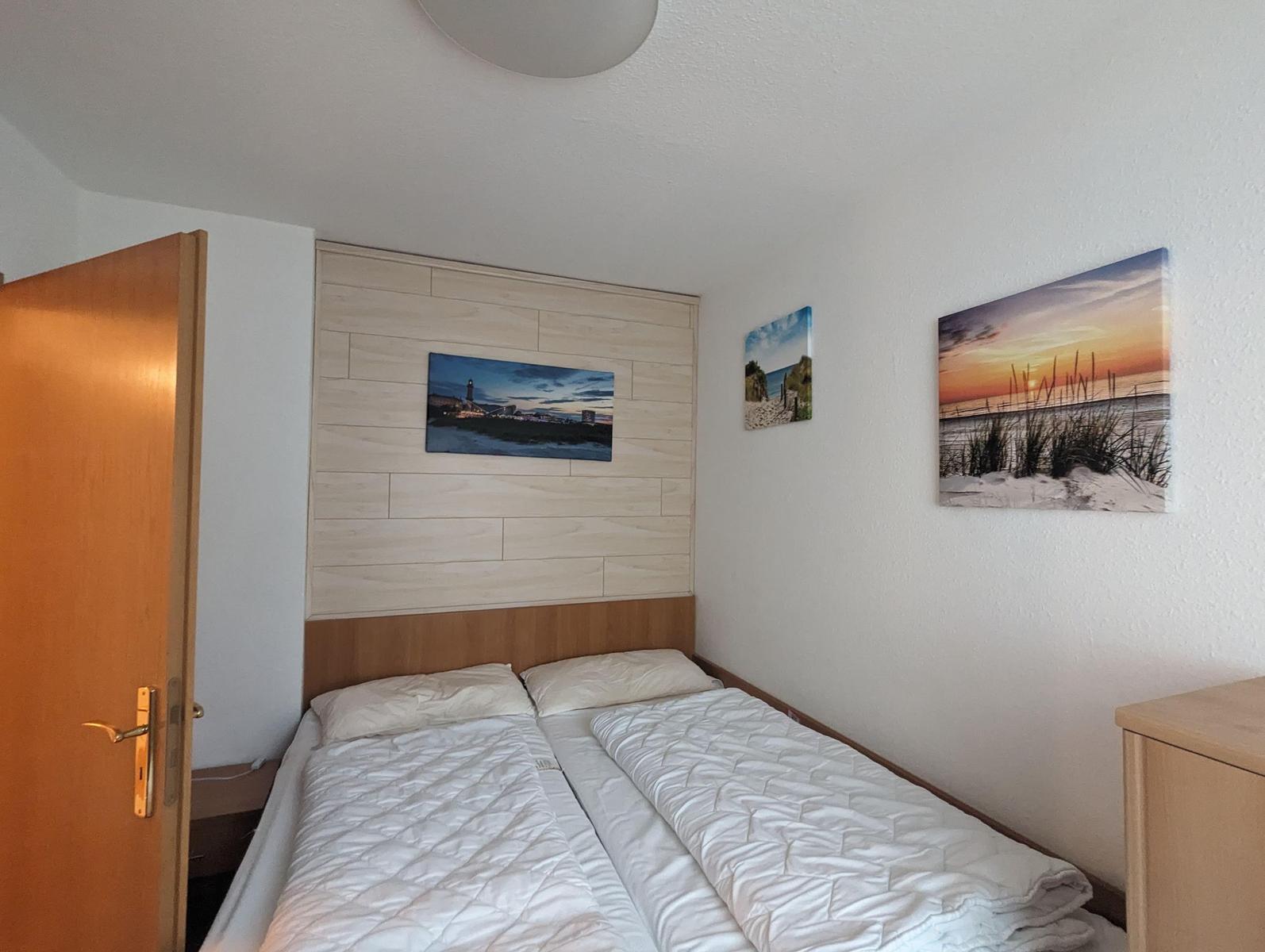 Schlafzimmer mit Doppelbett, Wandbildern und Holzelementen an der Wand.