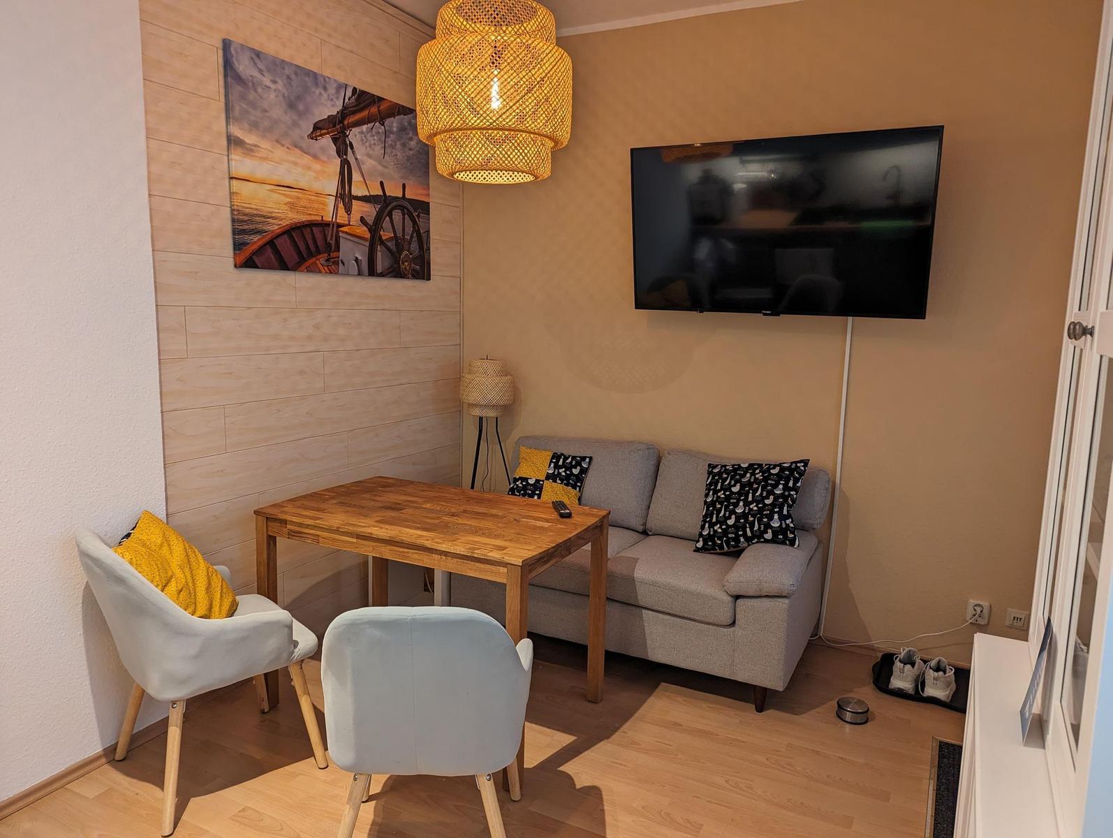 Wohnzimmer mit Sofa, Tisch, zwei Stühlen, Wandbild und Fernseher.