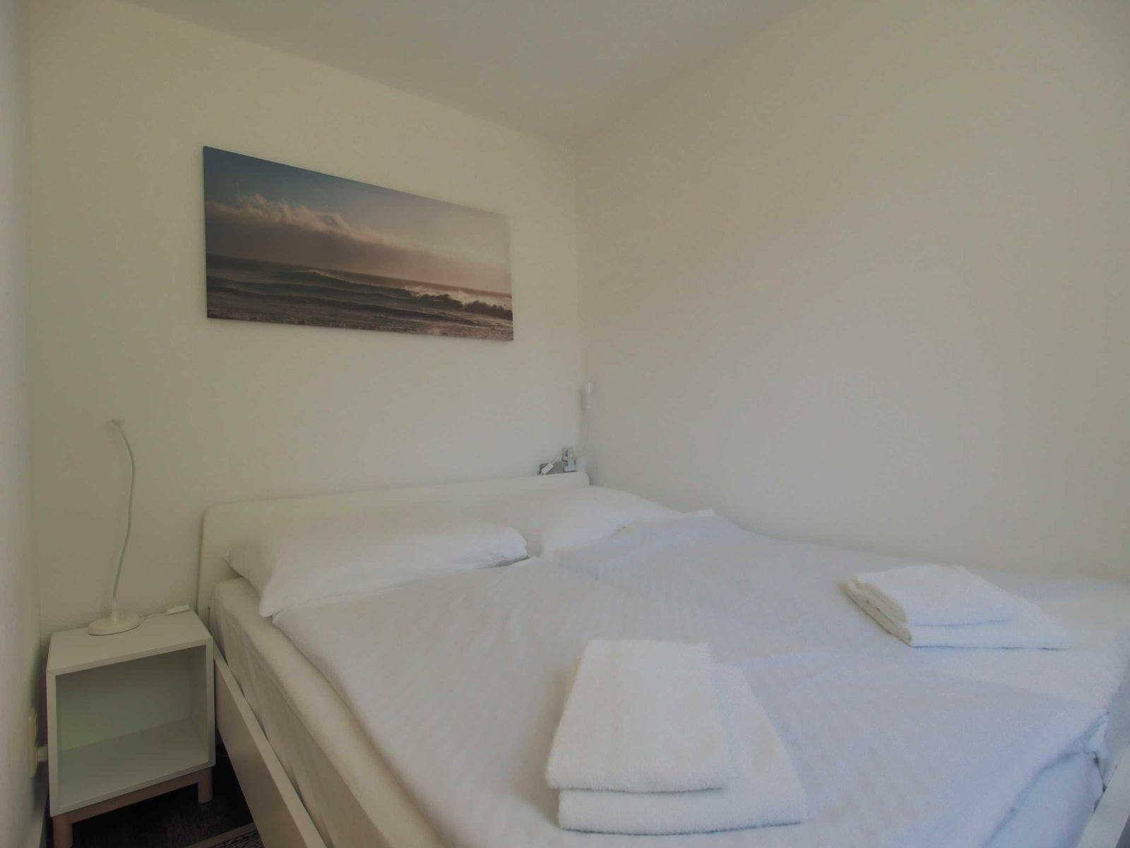 Ein Bett mit weißen Laken und Handtüchern. An der Wand hängt ein großes Bild.