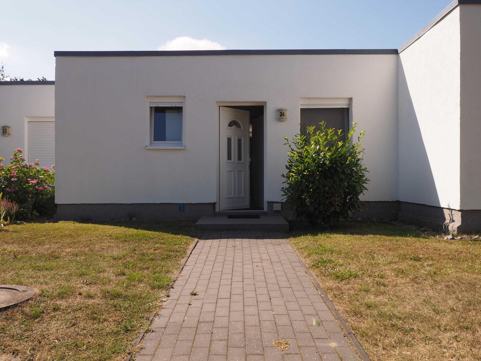 Haus mit weißen Wänden, Eingangstür und gepflastertem Weg.