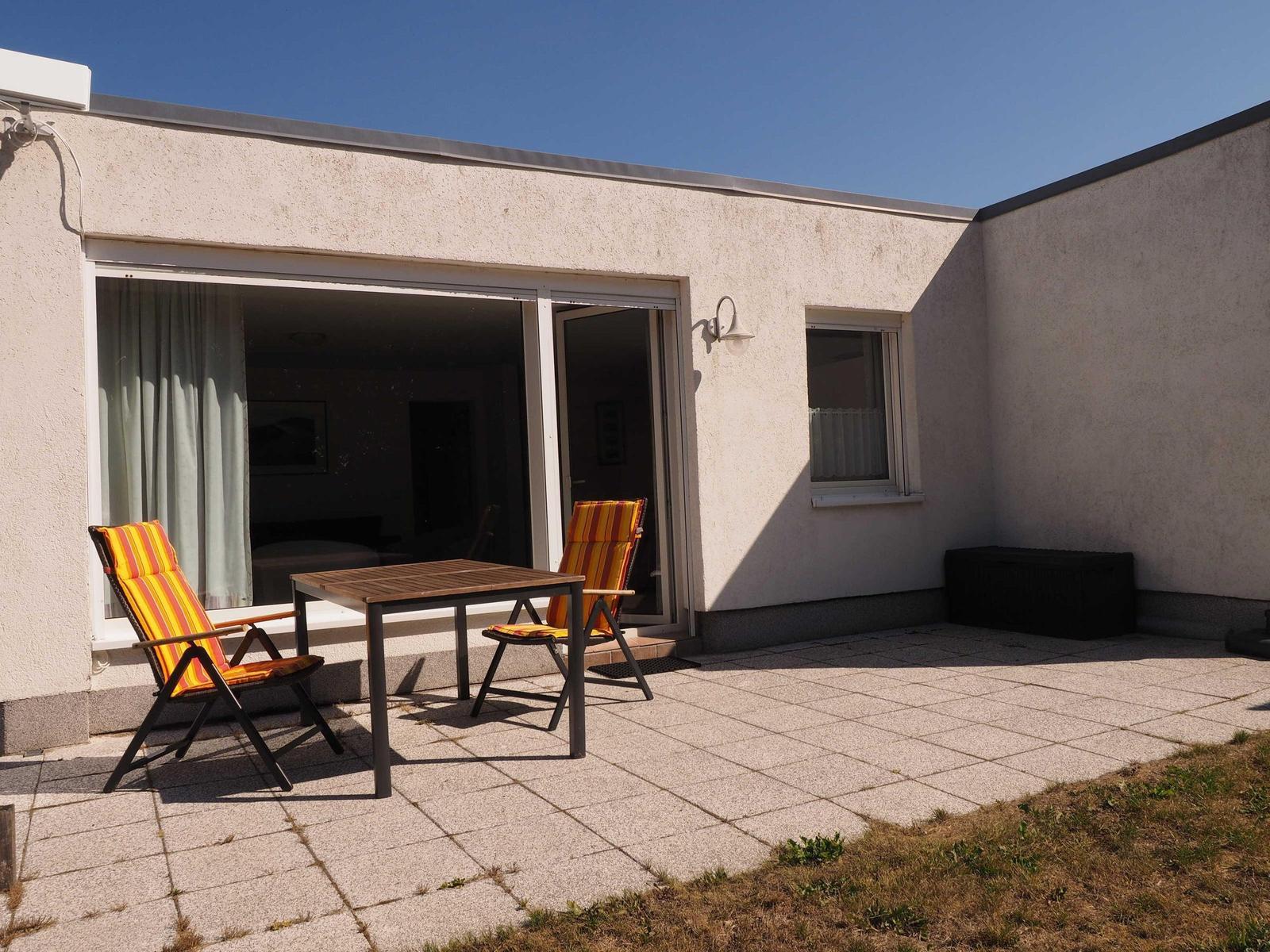 Terrasse mit Tisch und zwei Stühlen vor einem Haus mit Schiebetür.