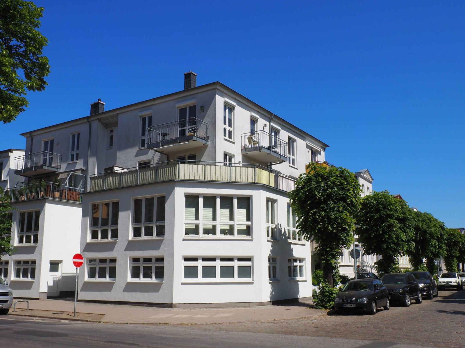 Wohnhaus mit Balkonen und Fenstern an sonnigem Tag.
