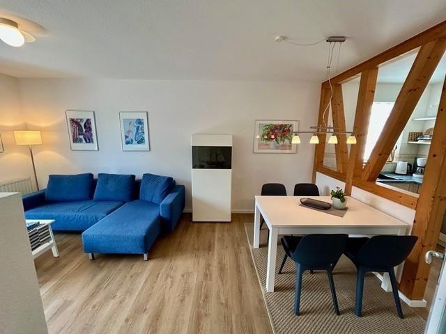 Wohn- und Essbereich mit blauem Sofa, Tisch und Stühlen, Holzboden und Sicht auf Küche.