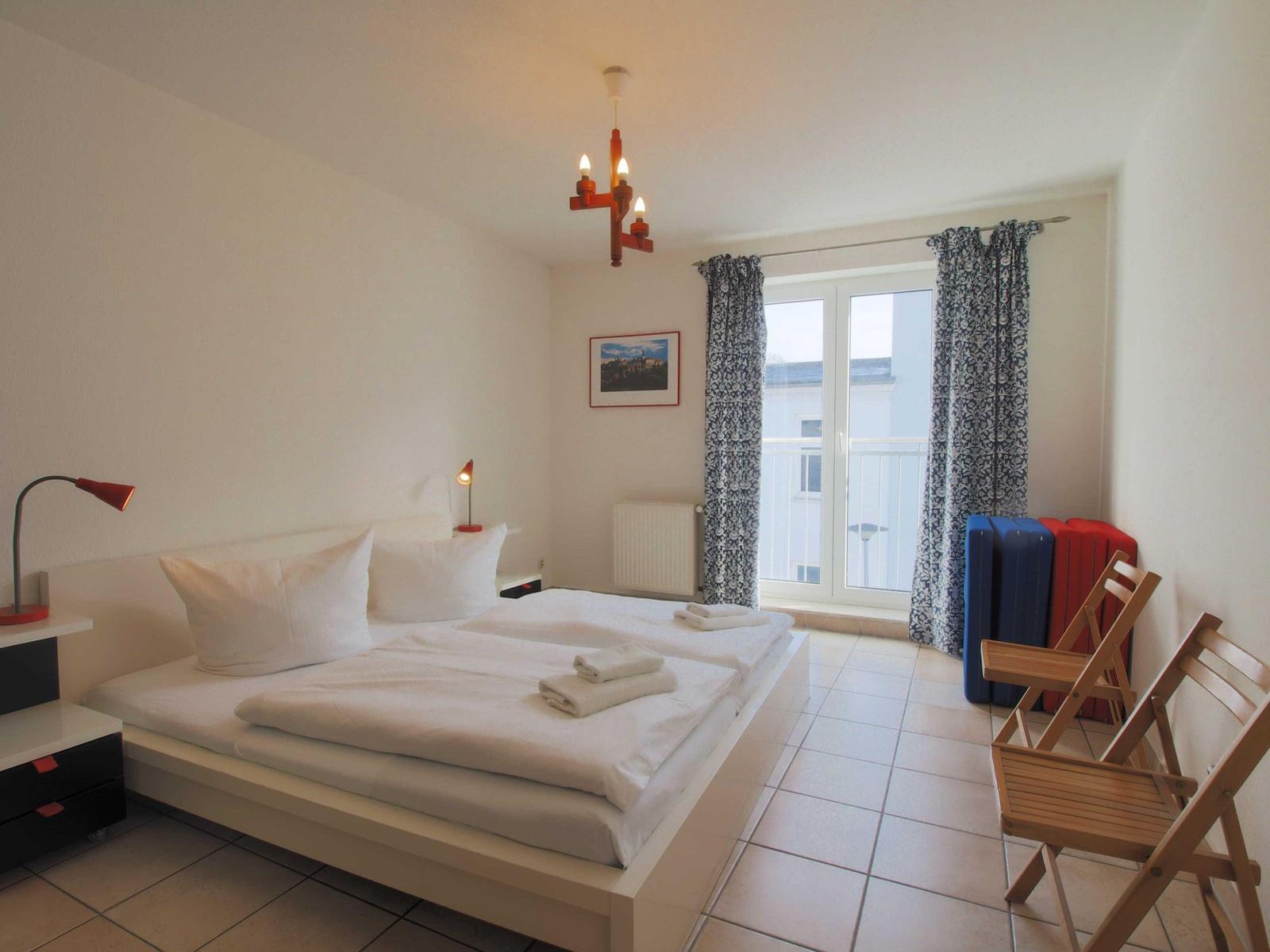 Schlafzimmer mit Doppelbett, Fenster, Stühlen und Kissen.