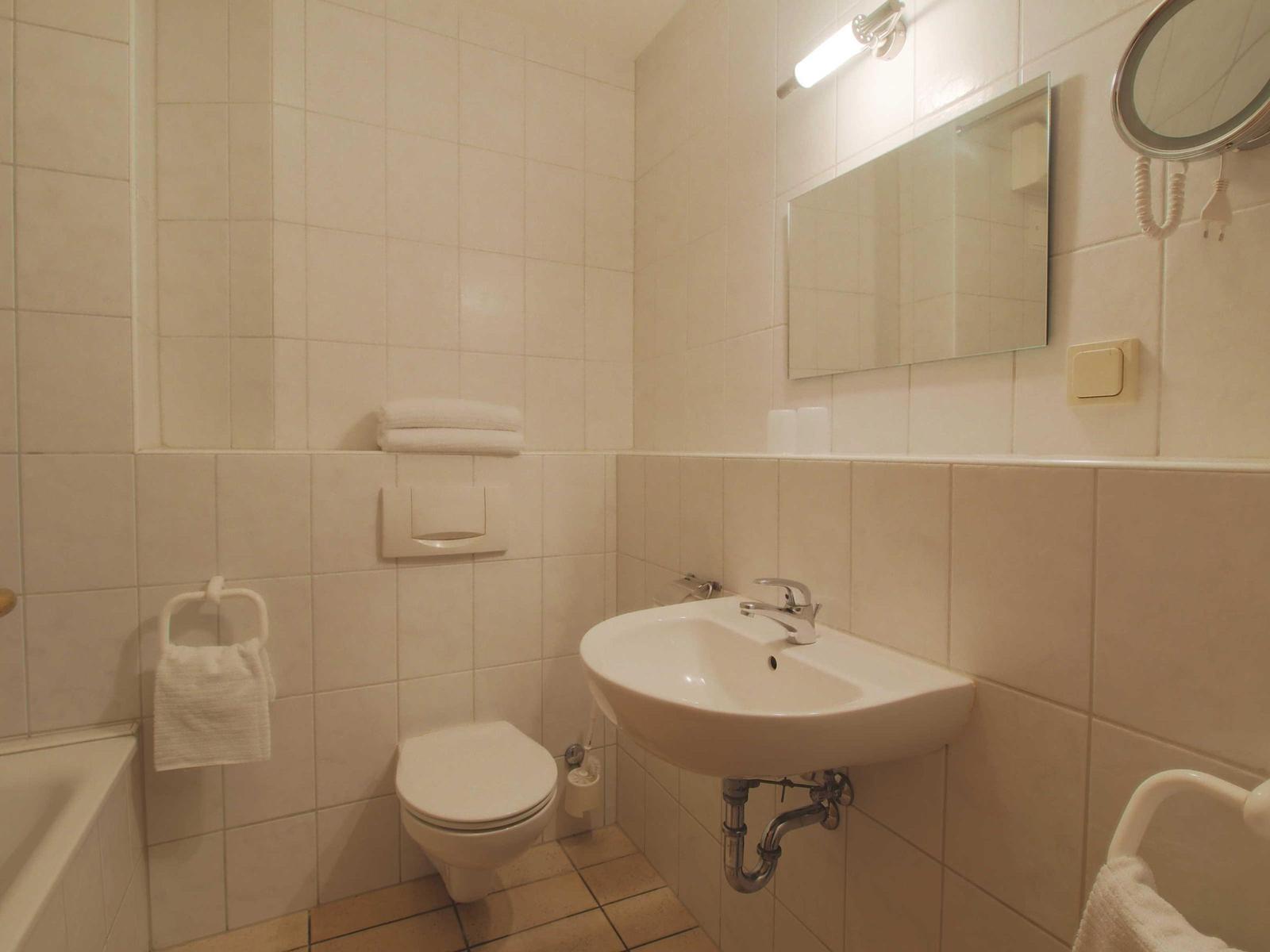 Badezimmer mit Waschbecken, Toilette, Spiegel und Handtuchhalter.