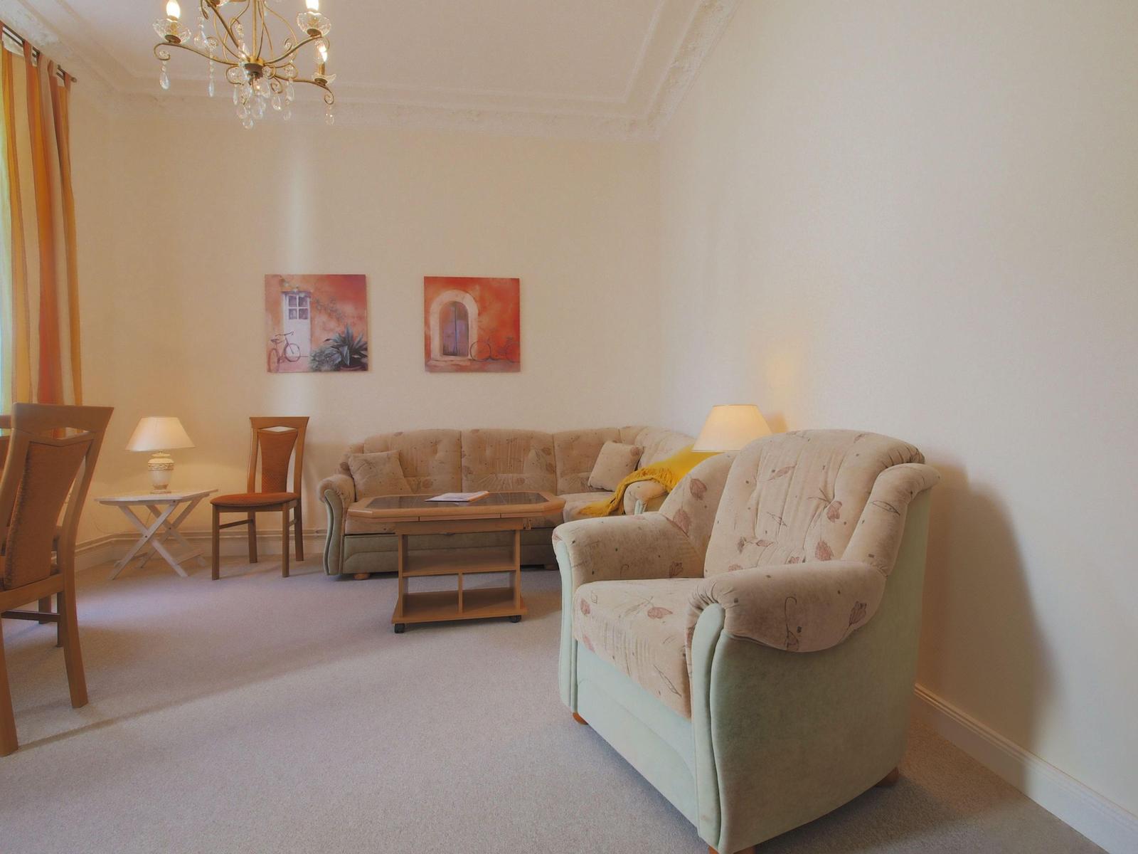 Wohnzimmer mit Sofa, Sessel, Tisch und Wandbildern.
