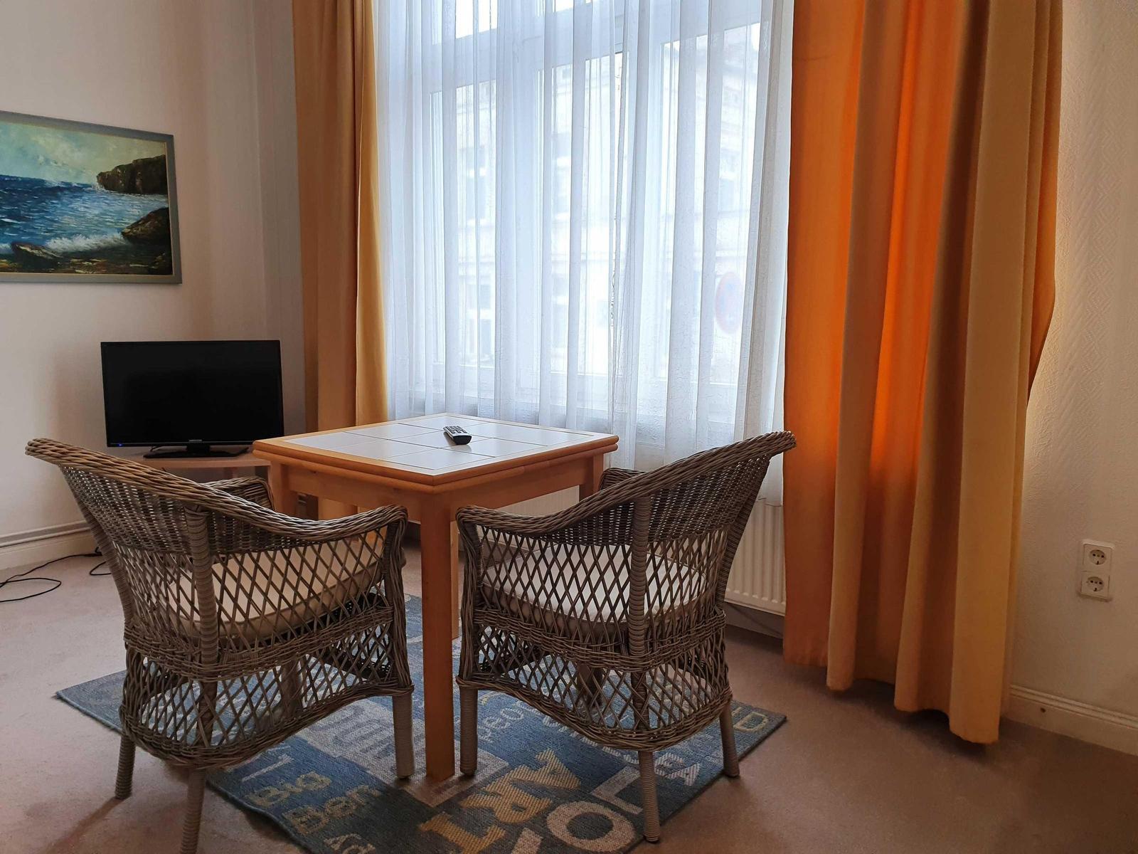 Zimmer mit Esstisch, zwei Stühlen, Fernseher und Fenster mit Vorhängen.