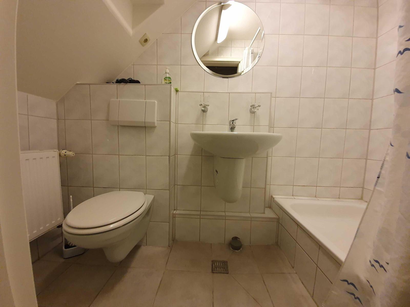 Badezimmer mit Toilette, Waschbecken und Badewanne unter Dachschrägen.