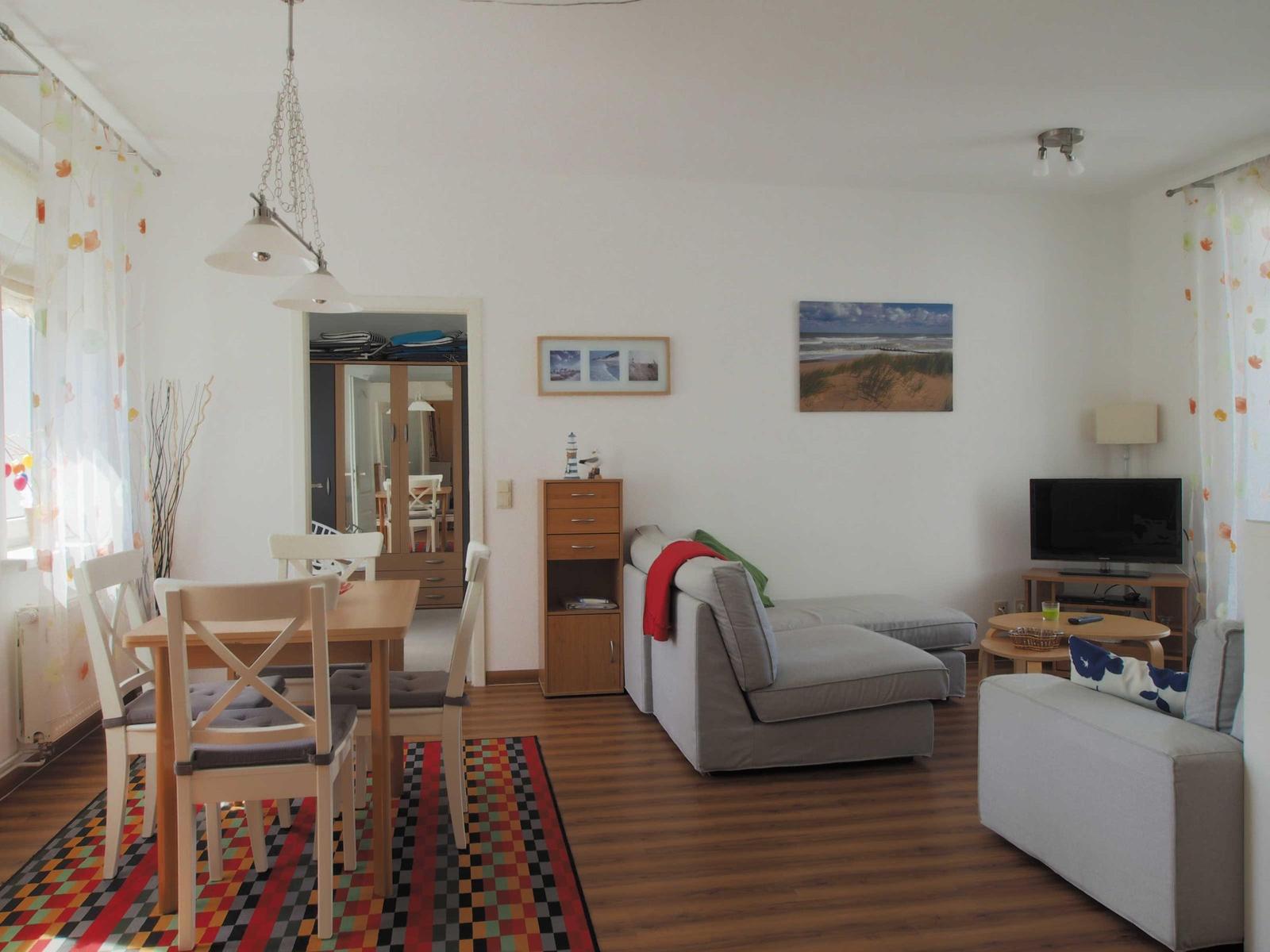 Wohn- und Essbereich mit Sofa, Tisch und Stühlen. Wandbild und TV sind sichtbar.