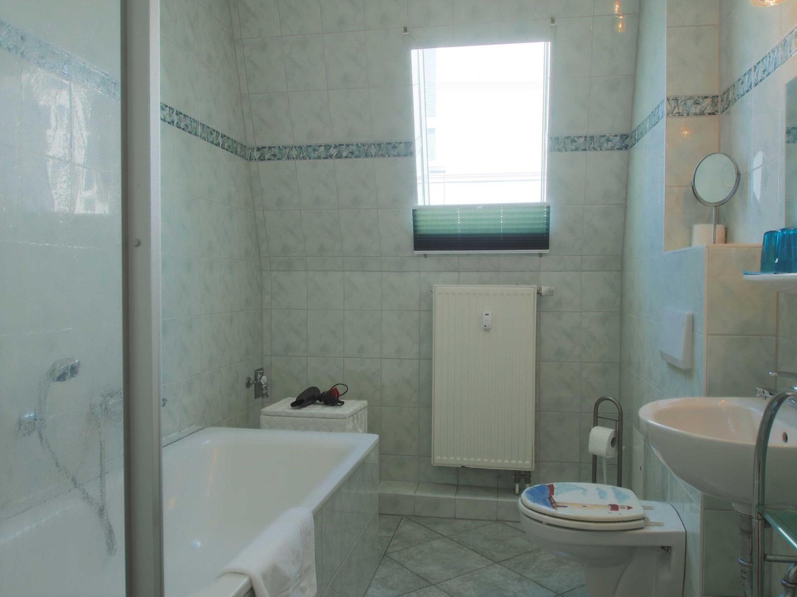 Badezimmer mit Badewanne, Dusche, Toilette und Waschbecken. Fenster mit Jalousie.