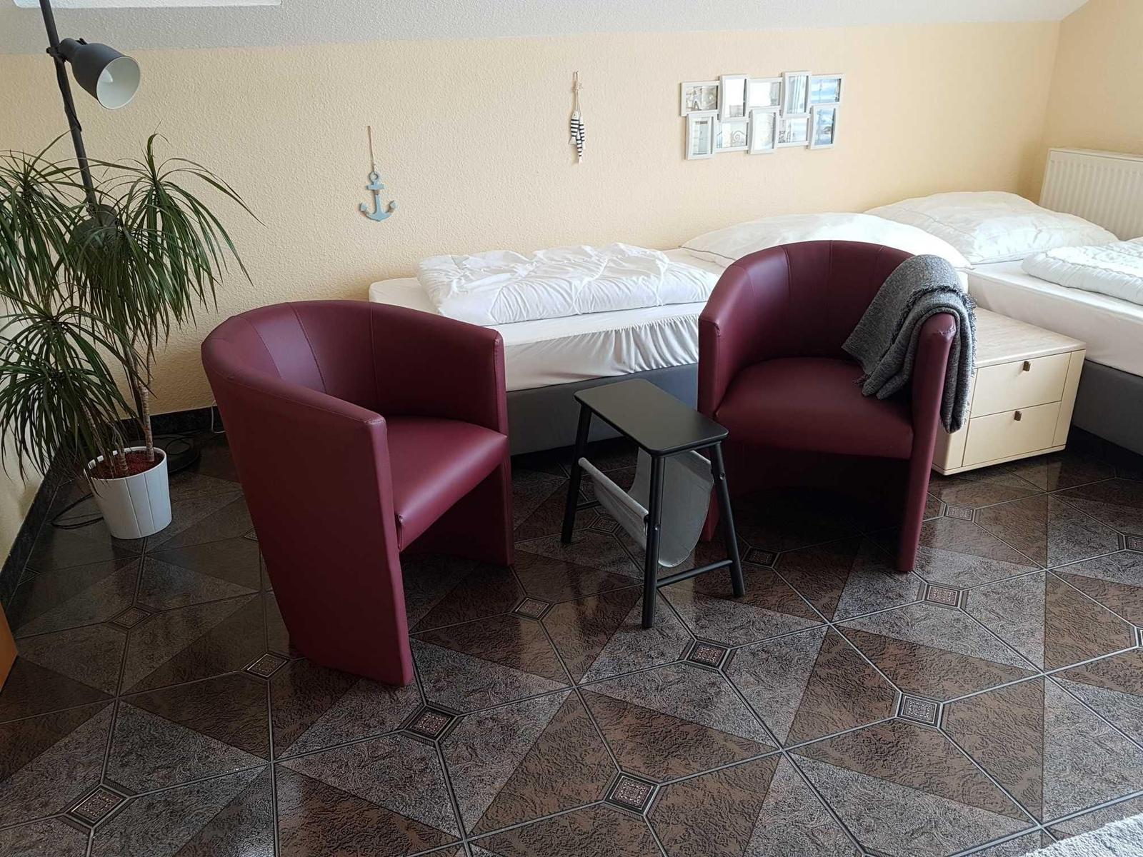 Zwei rote Sessel, ein kleiner Tisch, ein Bett und eine Pflanze im Raum.