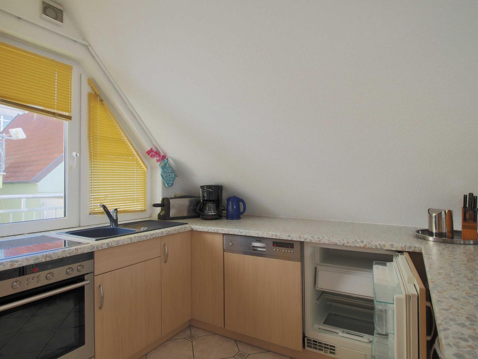 Küche mit Spüle, Herd, Kühlschrank und Waschmaschine unter Dachschräge.