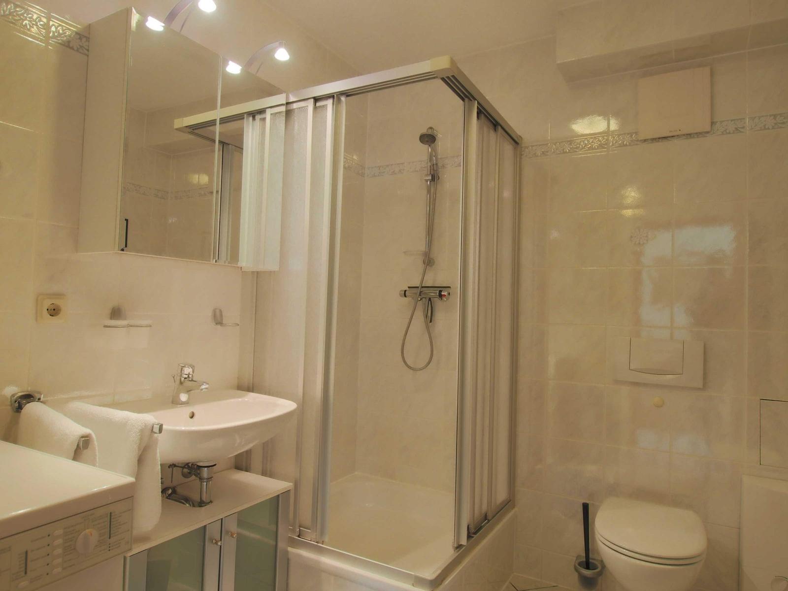 Badezimmer mit Dusche, Waschbecken und Toilette. Fliesen und Spiegel sichtbar.