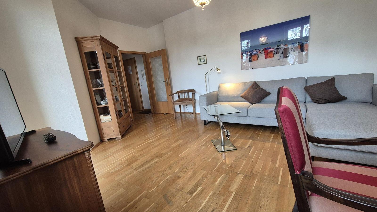Wohnzimmer mit Sofa, Glas-Tisch und Holzboden. Wandbild zeigt Strand.