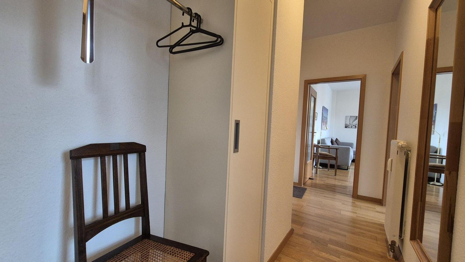 Flur mit Stuhl, Kleiderständer und Blick in Wohnzimmer mit Sofa.